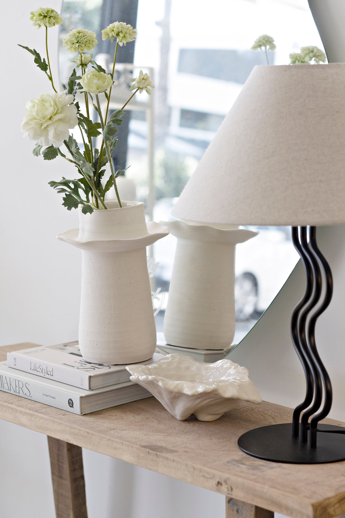 Recycled teak console with cream vases of white flowers, a wavy black lamp and a shell dish