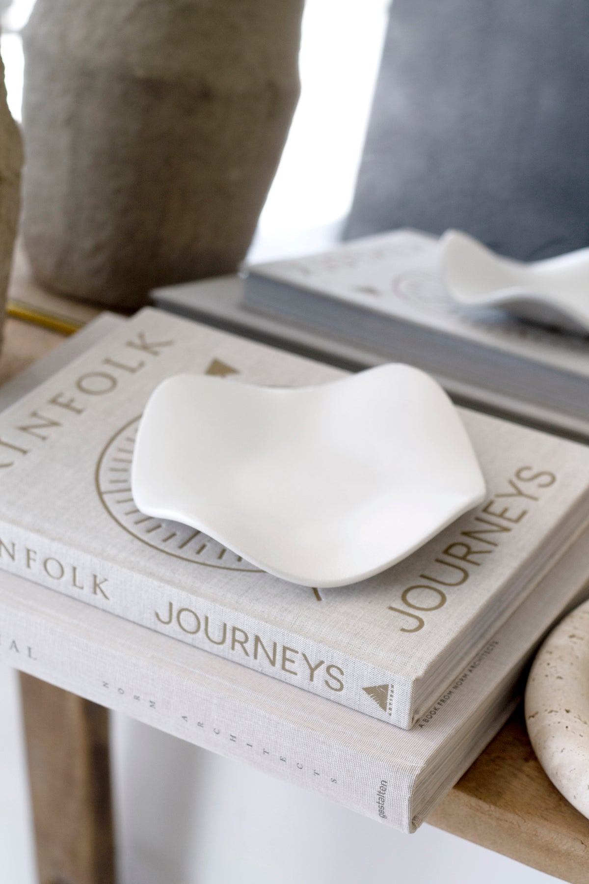 White wave tray resting on a stack of coffee table books on a timber console beside an aged stone vase