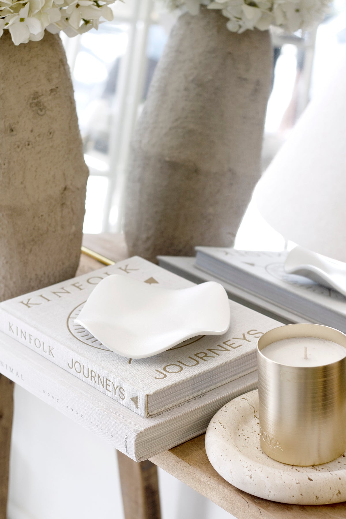 White wave tray on stacked books with a brushed gold candle on a travertine dish and dried white hydrangeas