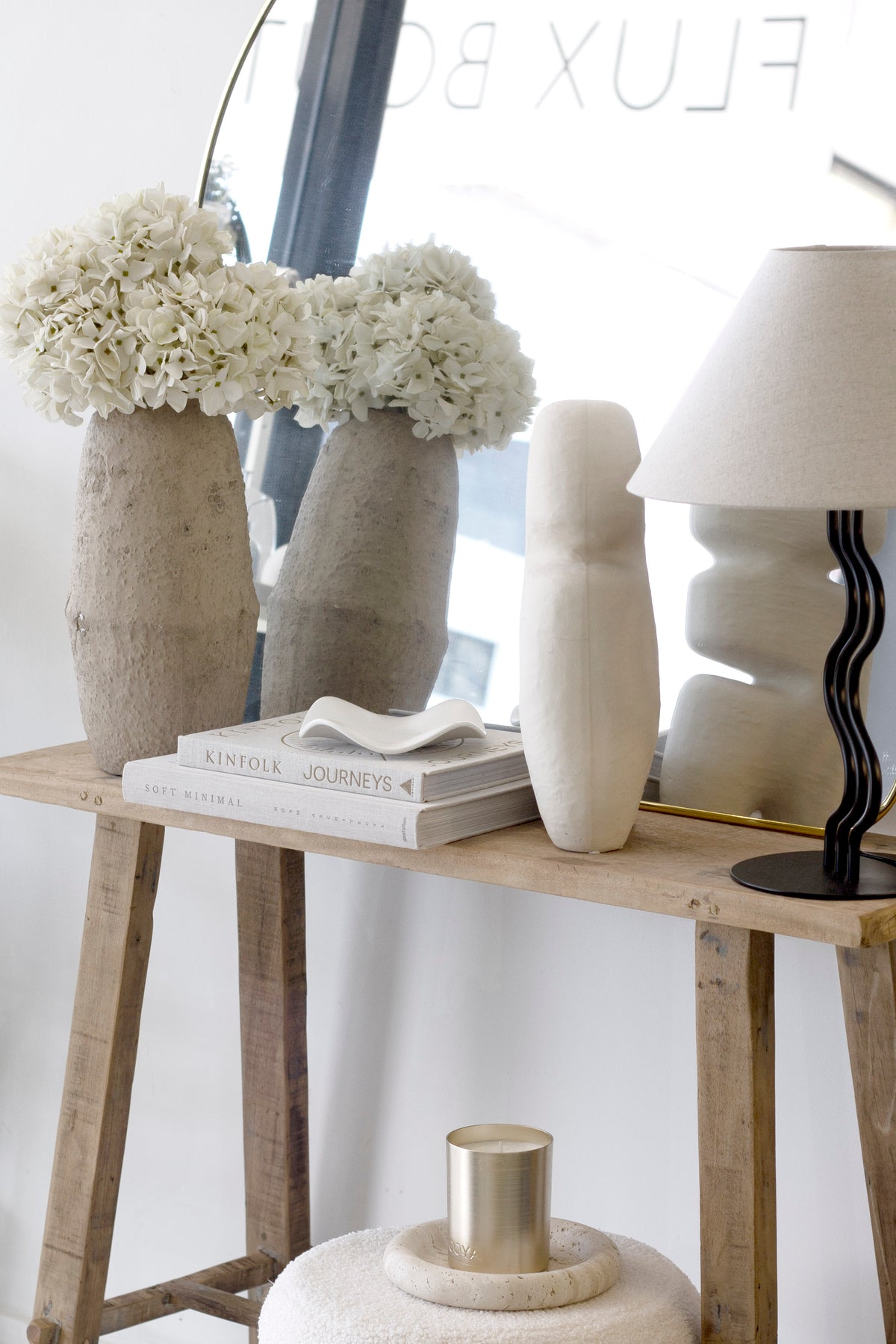 Console styled with stone vases of white hydrangeas, a sculptural vase, a wavy-stem lamp and the white wave tray