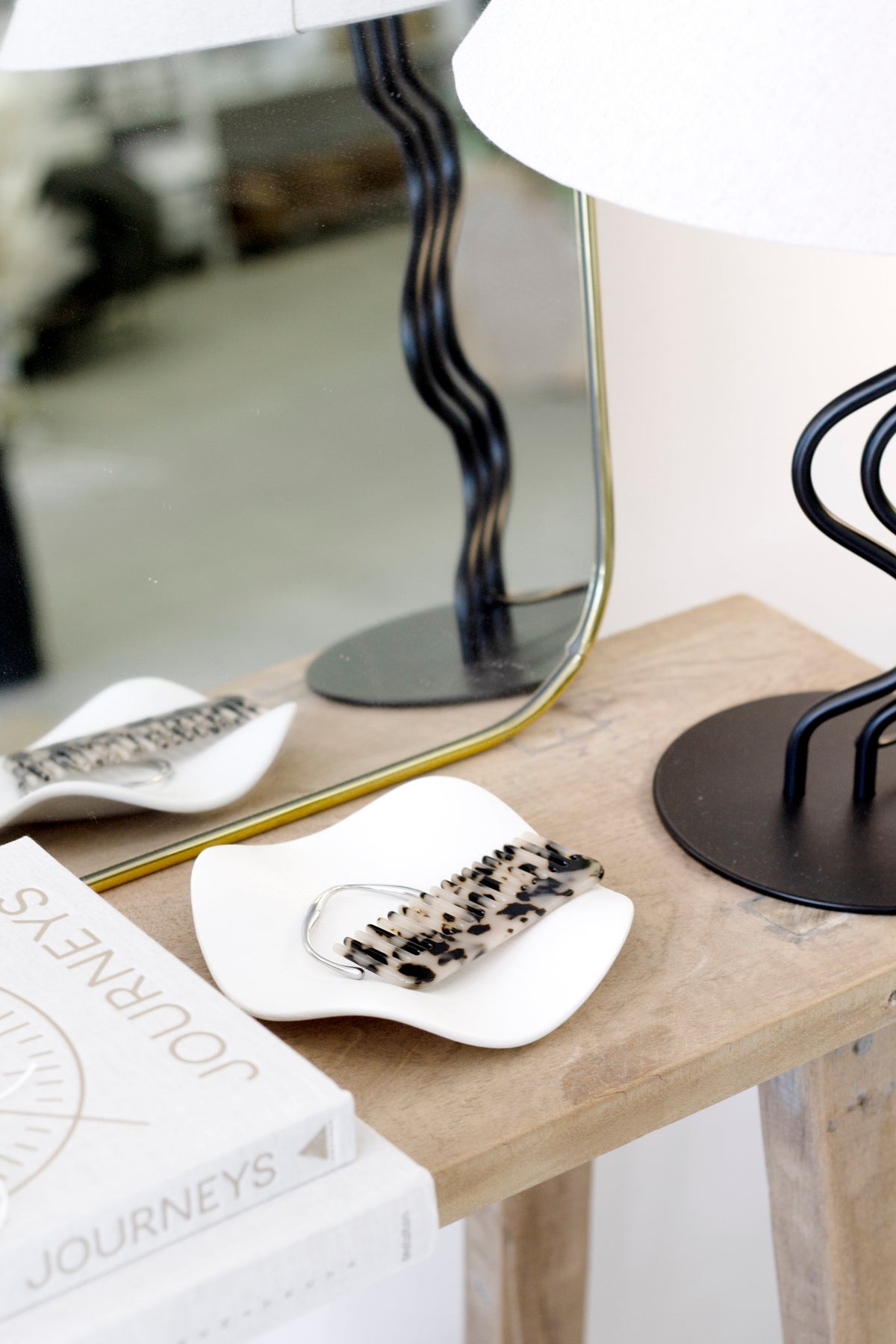 Two white wave trays on a timber console, one holding a speckled tortoiseshell hair clip, mirror behind