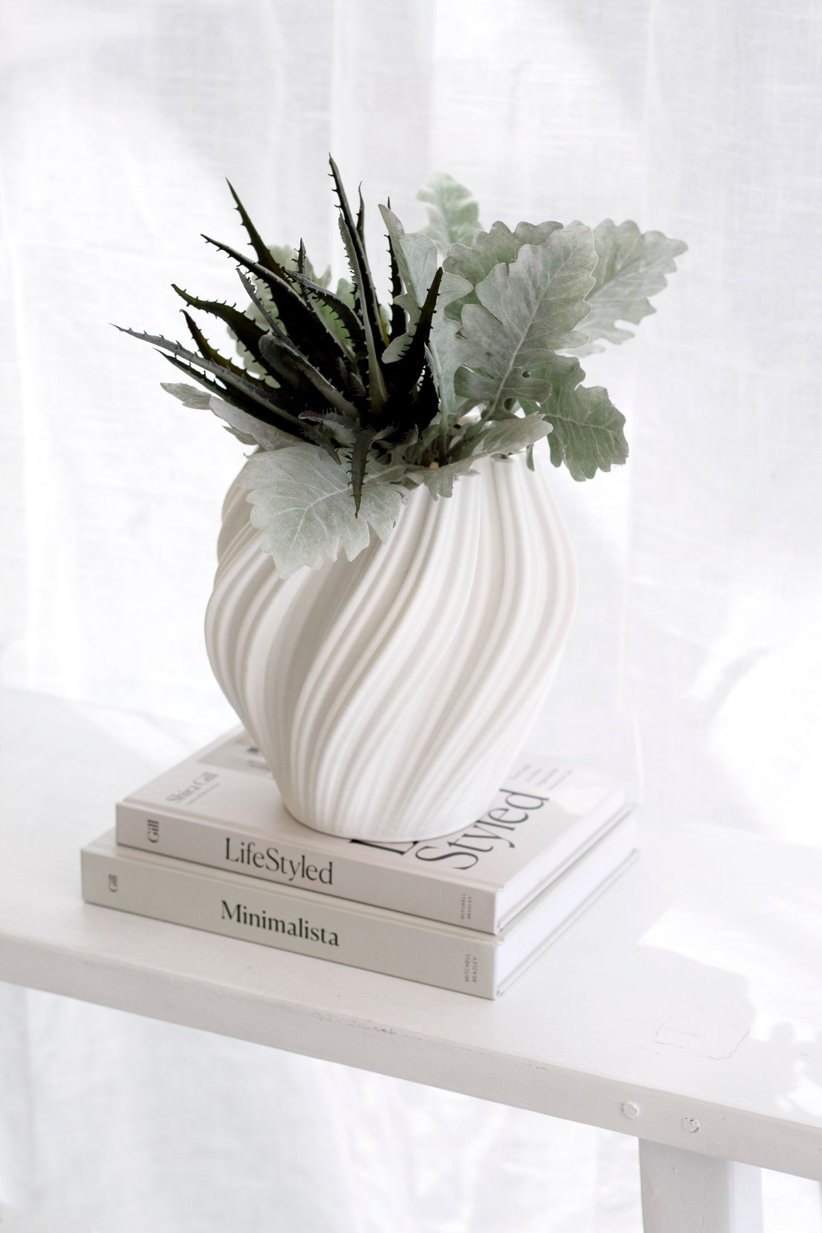 White Amelie fluted vase with succulent and dusty miller foliage on stacked books