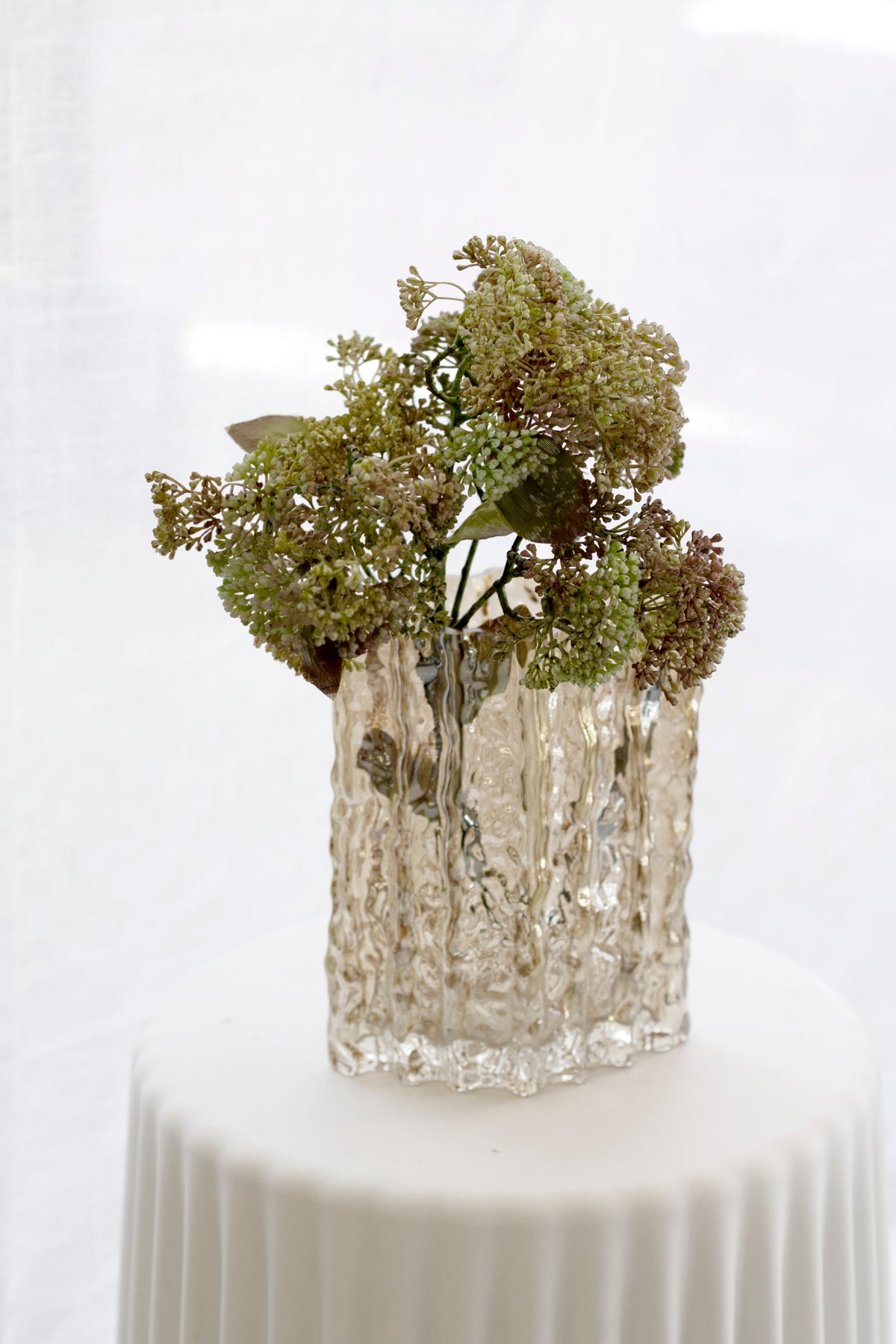 Gold Glacier vase holding dried hydrangea on a fluted white pedestal