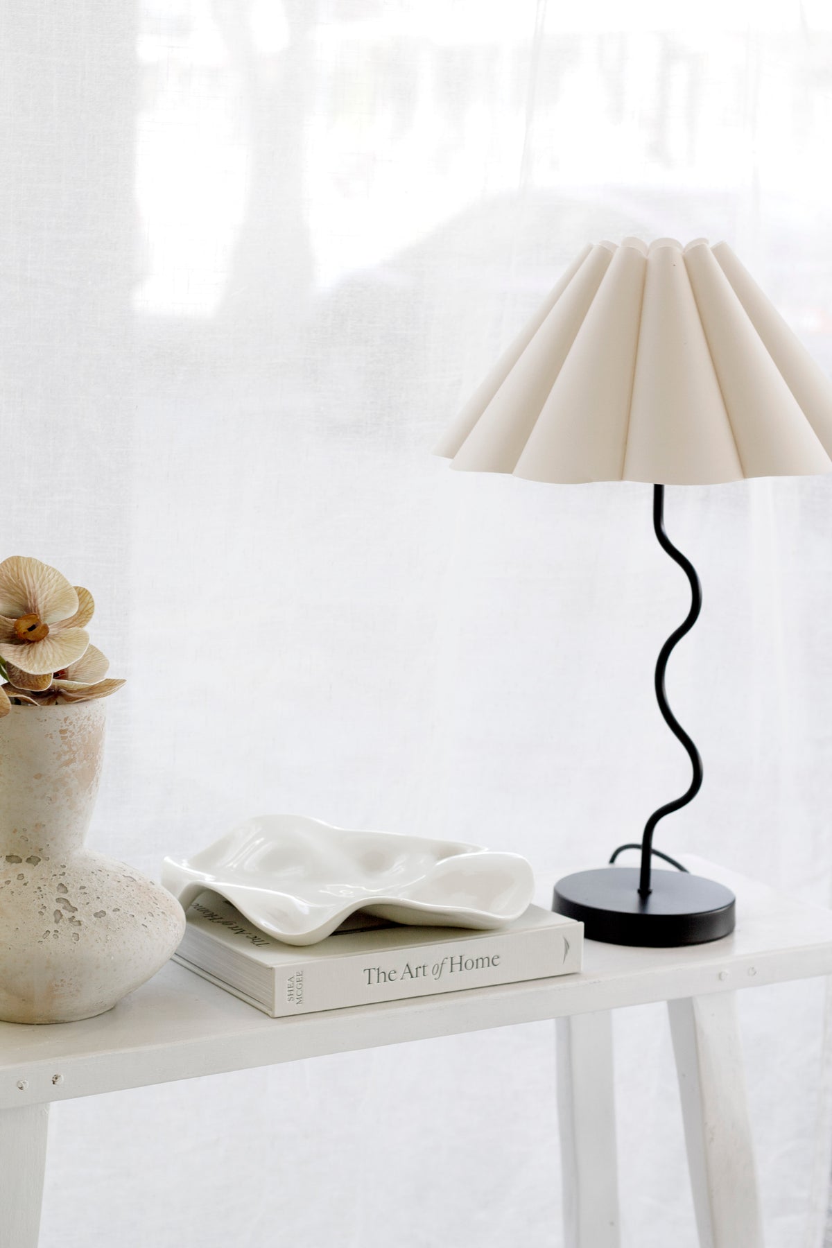 Black wavy table lamp on a white console beside a scalloped ceramic dish