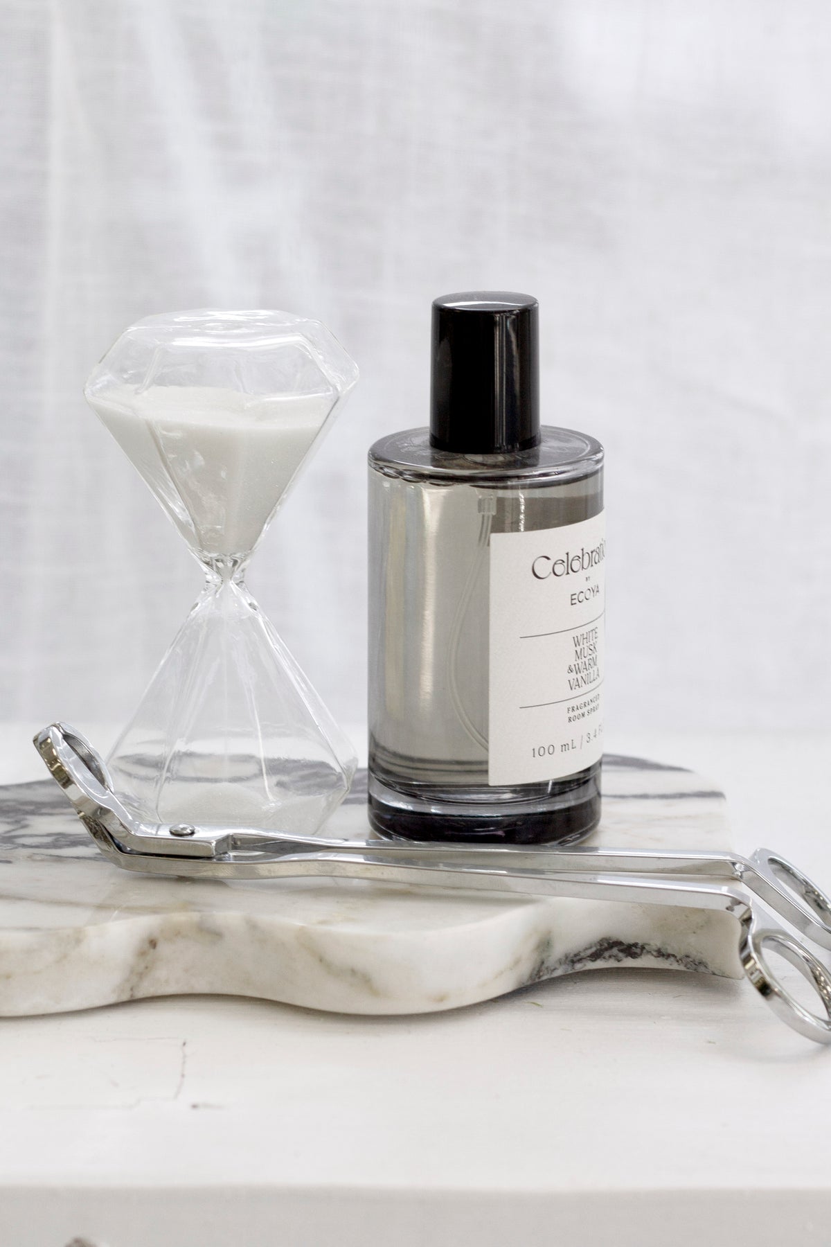 Silver wick trimmer on a marble wave tray with an hourglass and a fragrance bottle