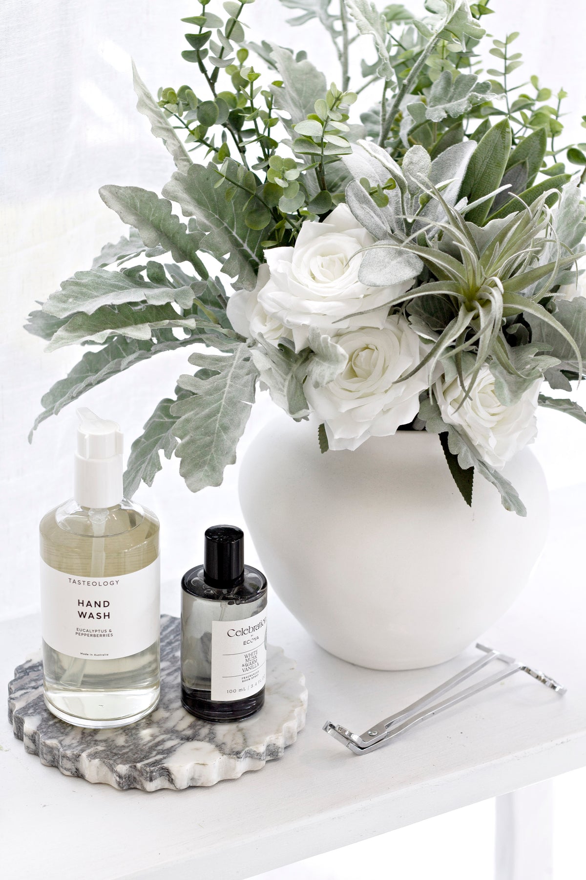 Celebration diffuser on a marble tray with bottles beside a white vase of flowers and greenery