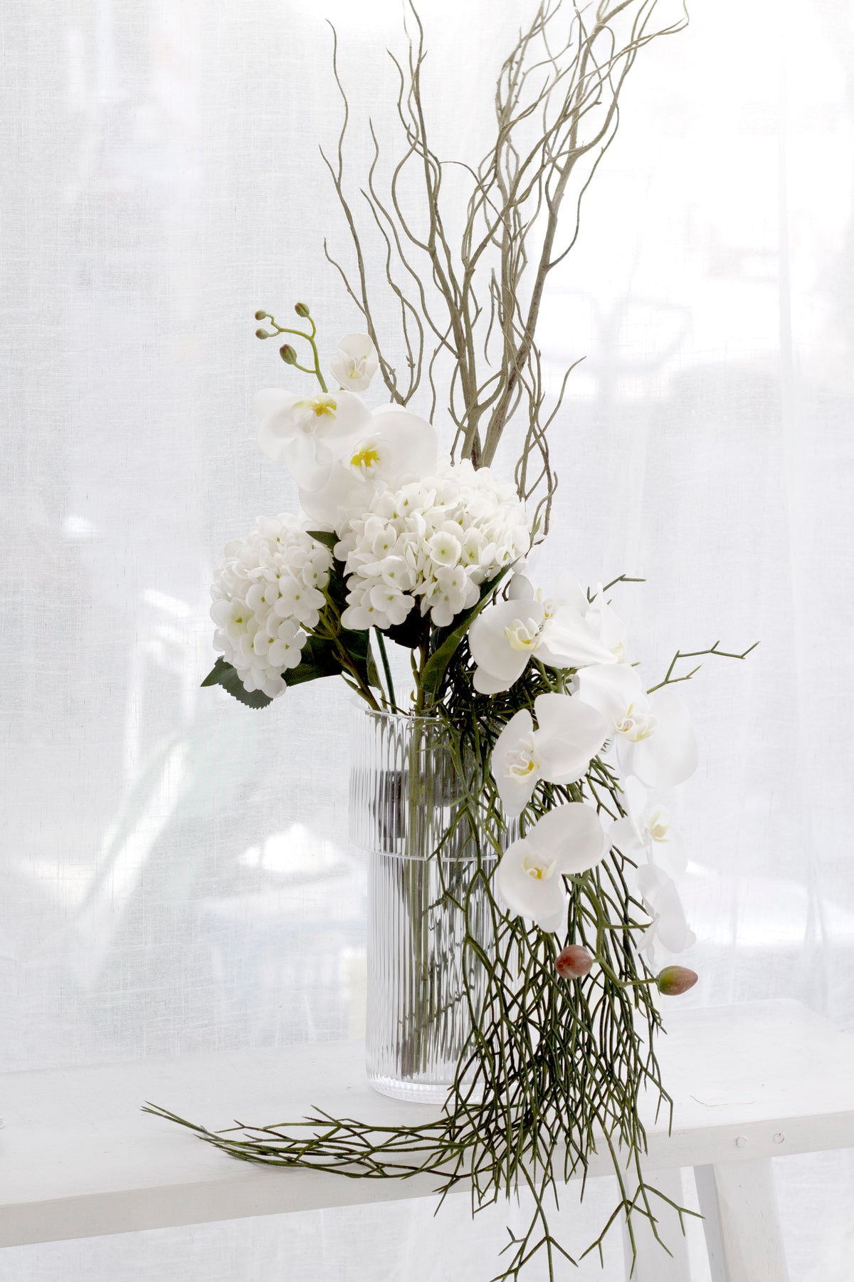 Faux rhipsalis trailing from a vase of white flowers by a window