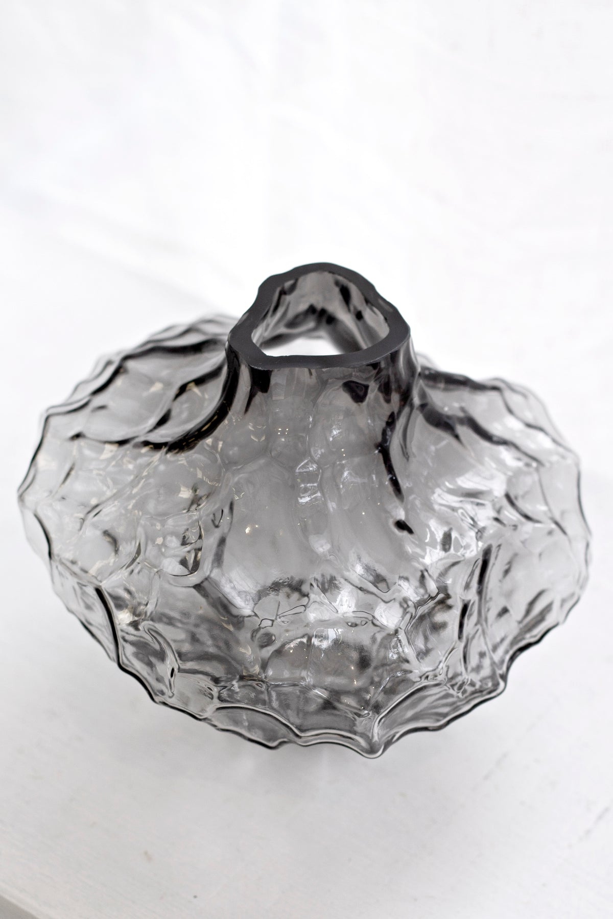 Smoky black rippled crystal glass vase on a pale background, showing the textured surface
