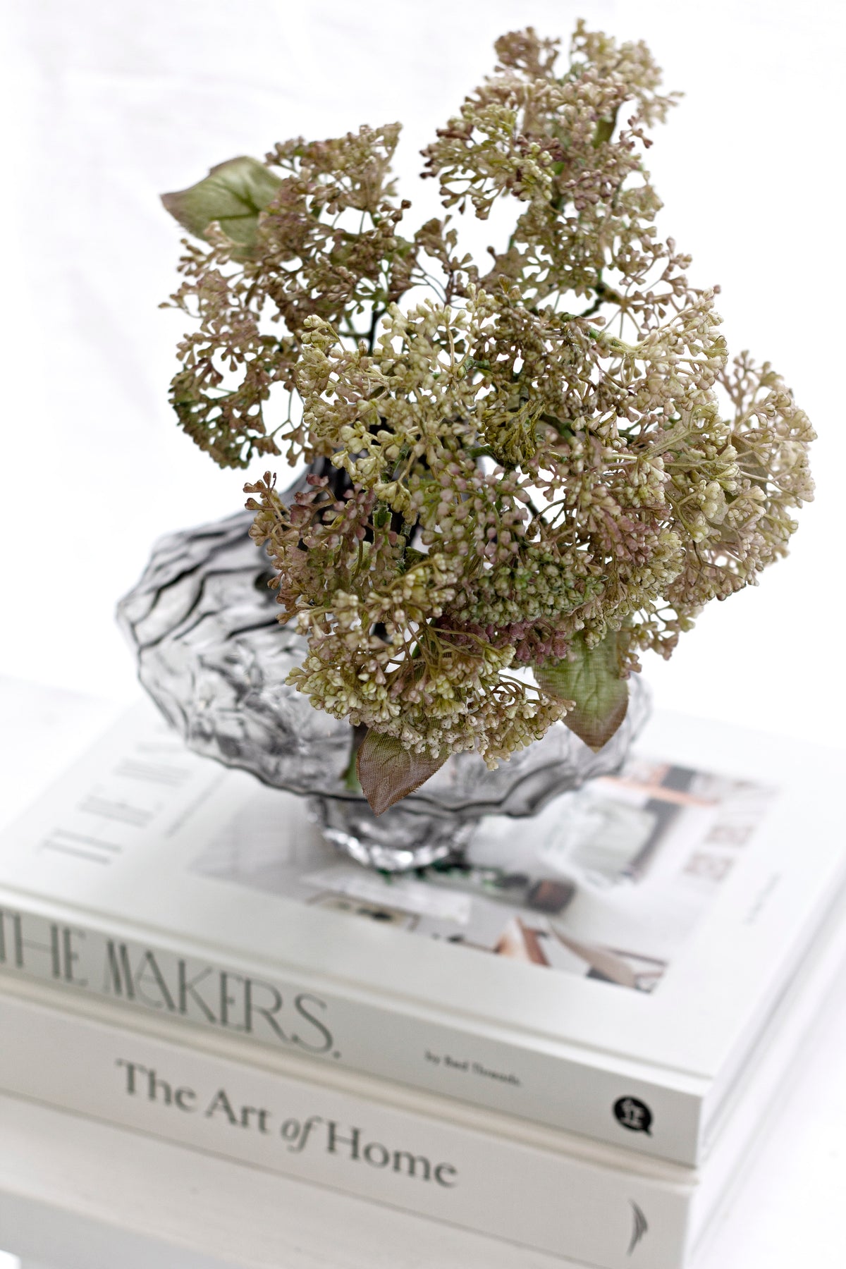 Clear rippled crystal glass vase holding dried hydrangea on a stack of coffee table books