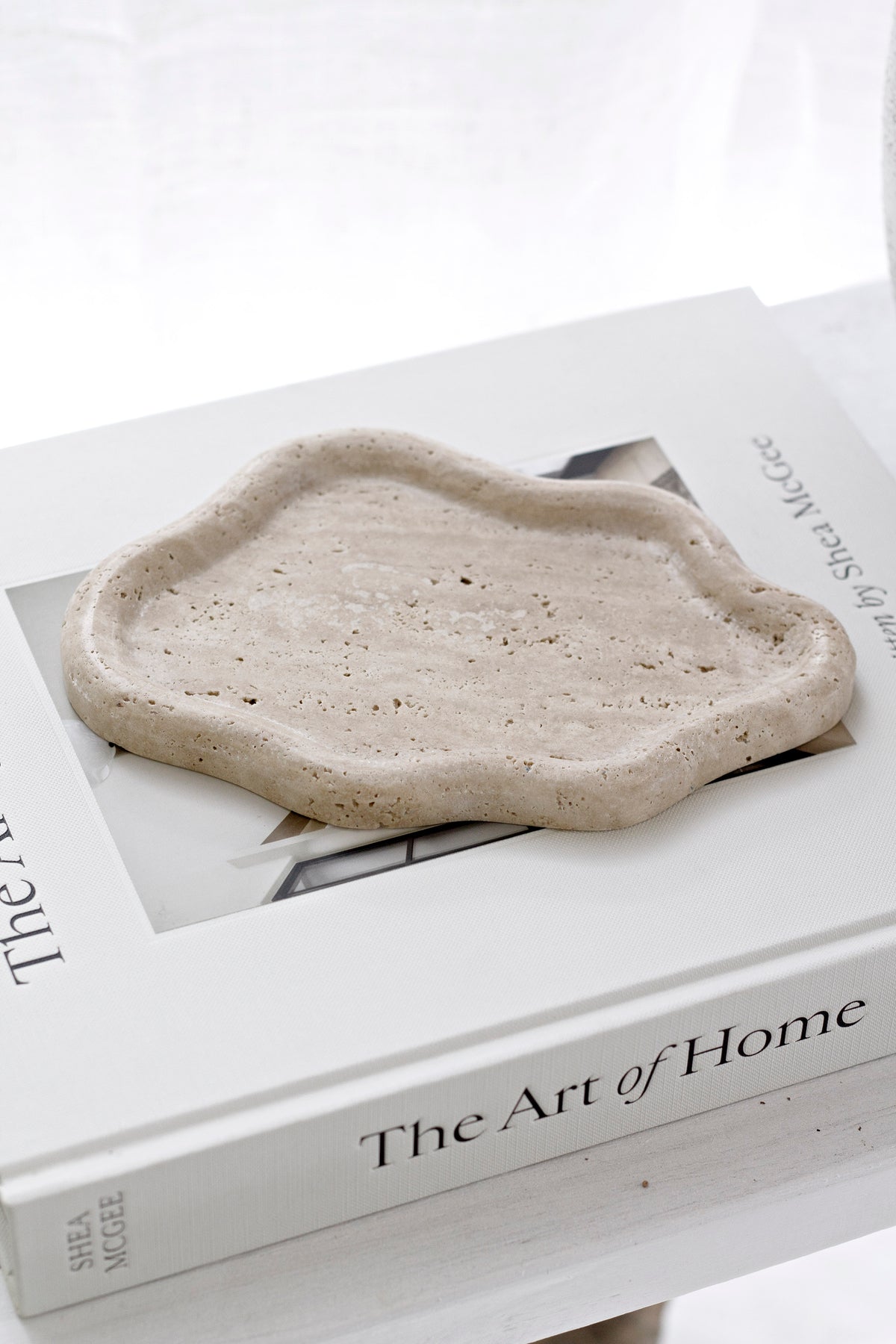 Close on the travertine catchall tray on a book stack, pitted stone in full view