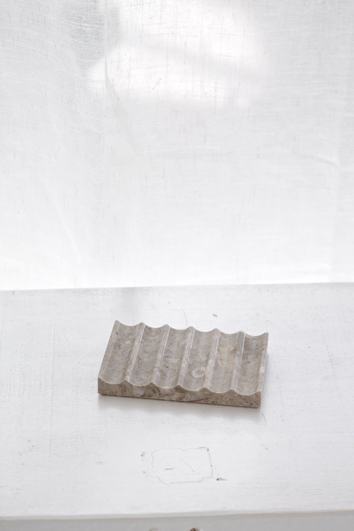 Fluted travertine tray on a white-painted ledge, soft shadow falling across the ridged stone