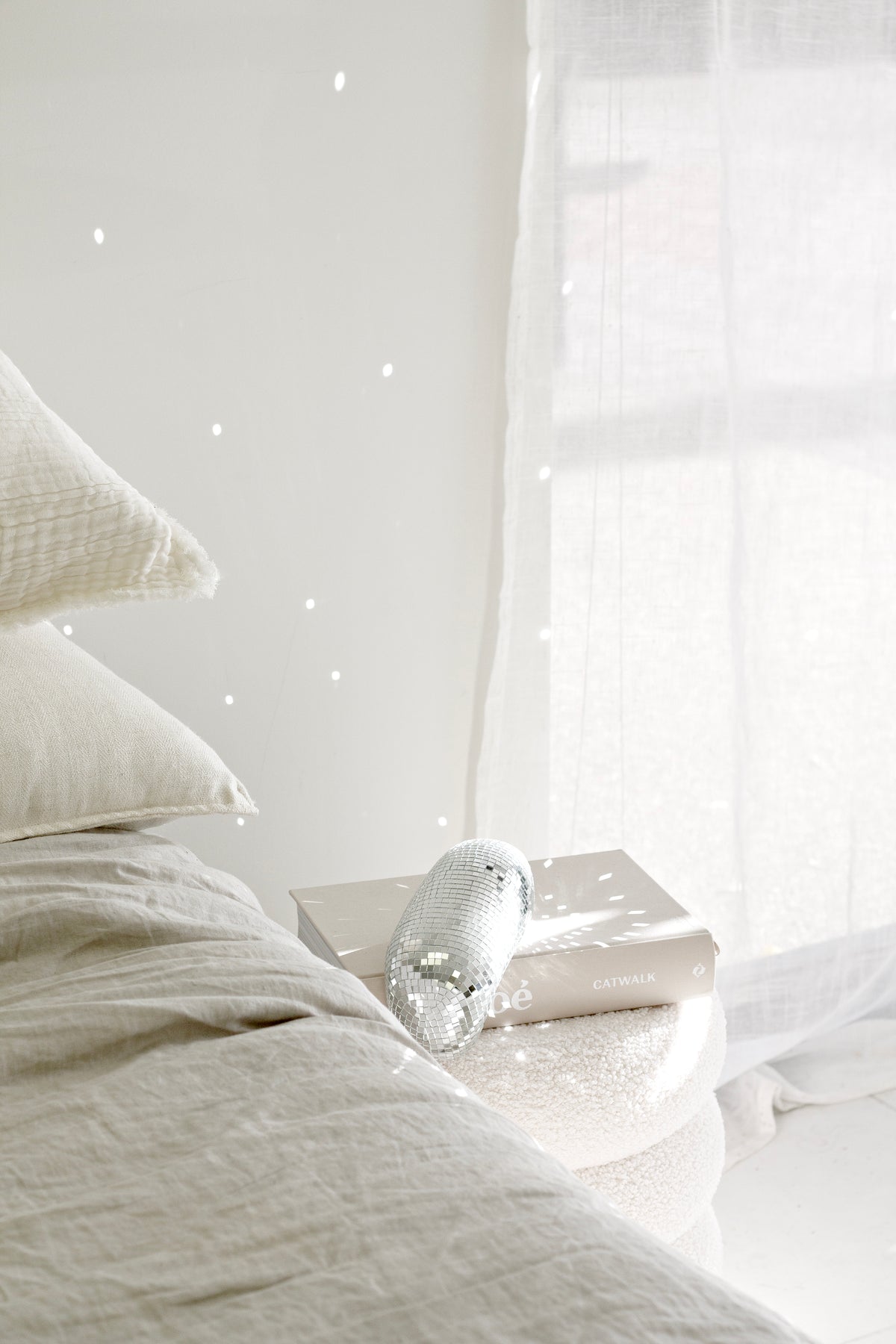 Melting disco ball resting on white bedding beside a sheer curtain