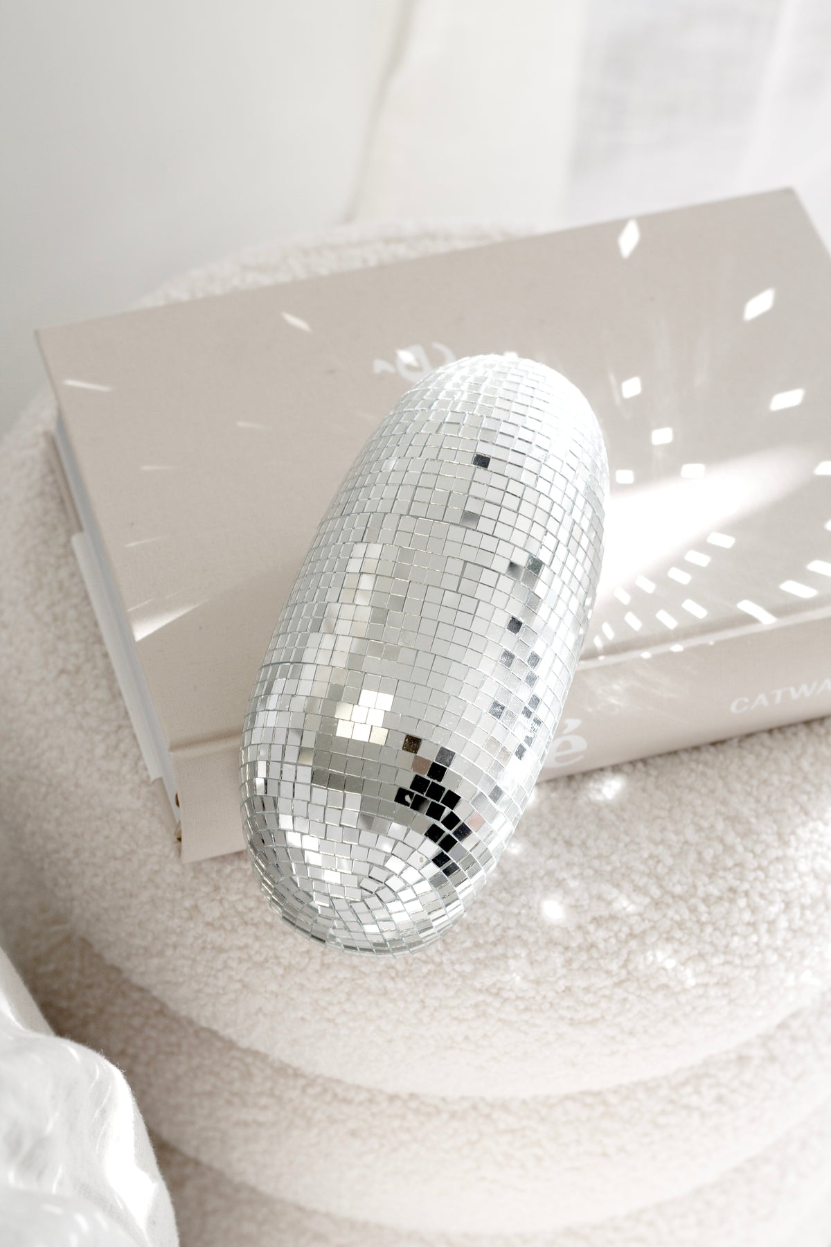 Silver disco ball resting in the hollow of the white boucle ottoman