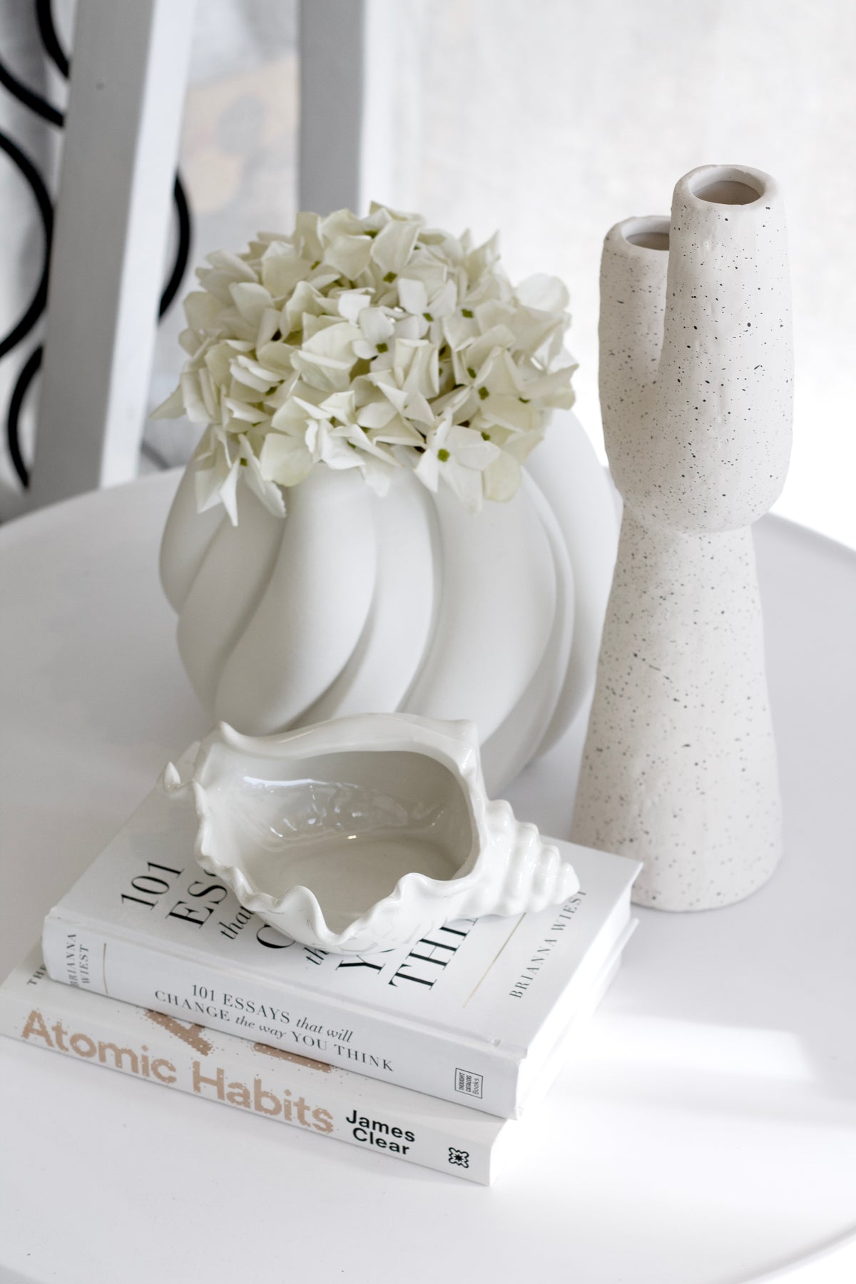 Franki vase beside white hydrangeas in a sculptural vase on a stack of books