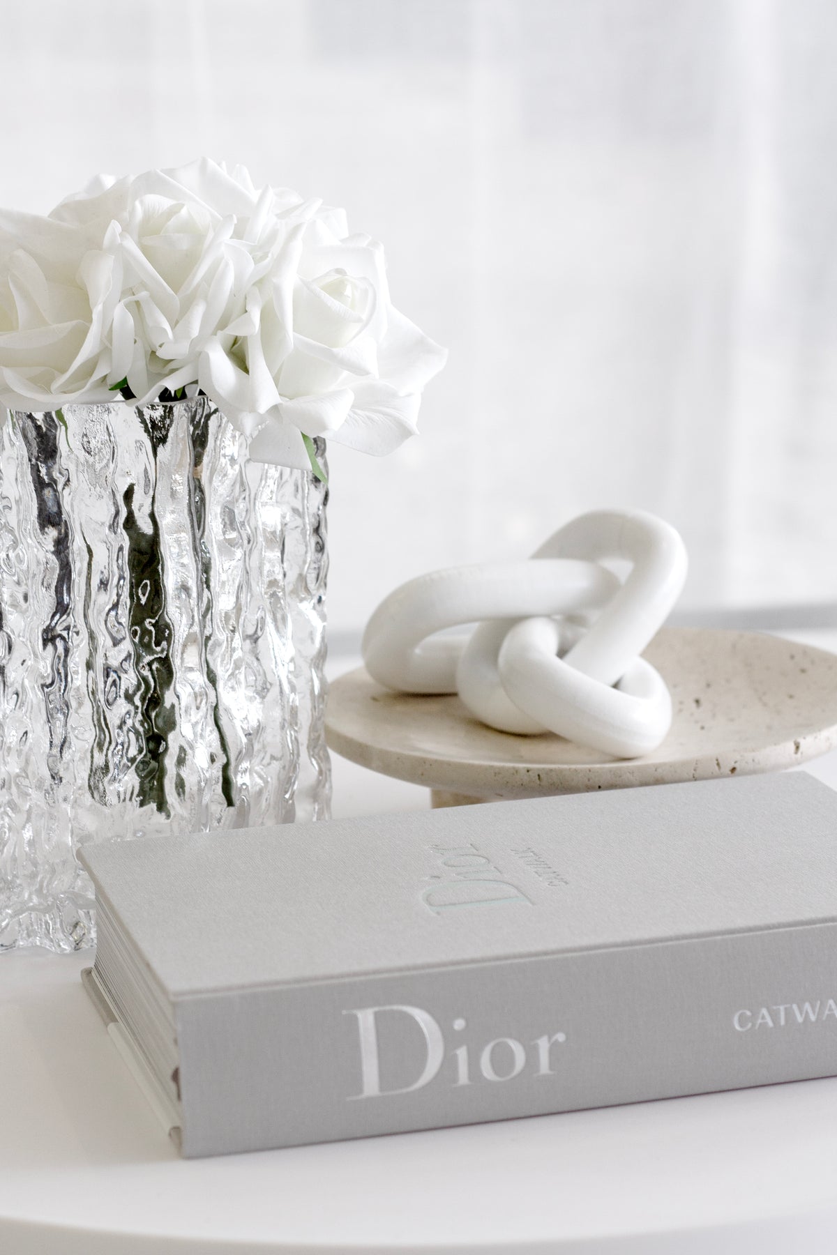 White wooden chain on a stone tray beside white roses in a textured glass vase