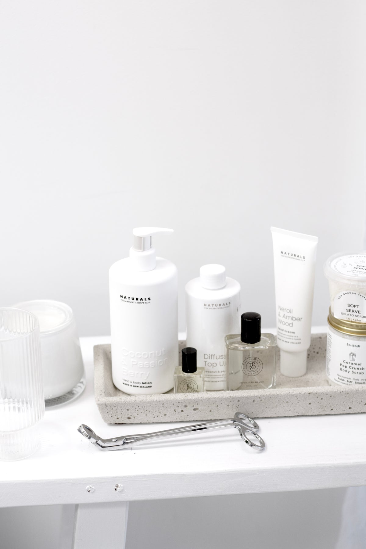Silver wick trimmer on a white counter below a stone tray holding skincare bottles