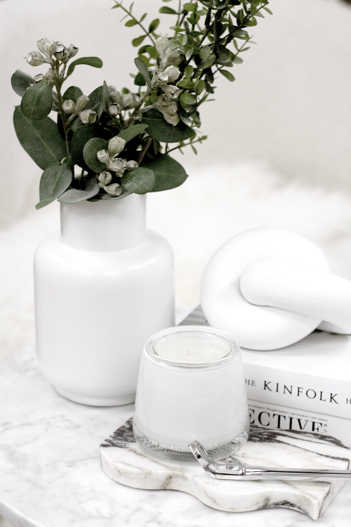 Matte white Flora vase holding eucalyptus beside a white knot ornament and a candle