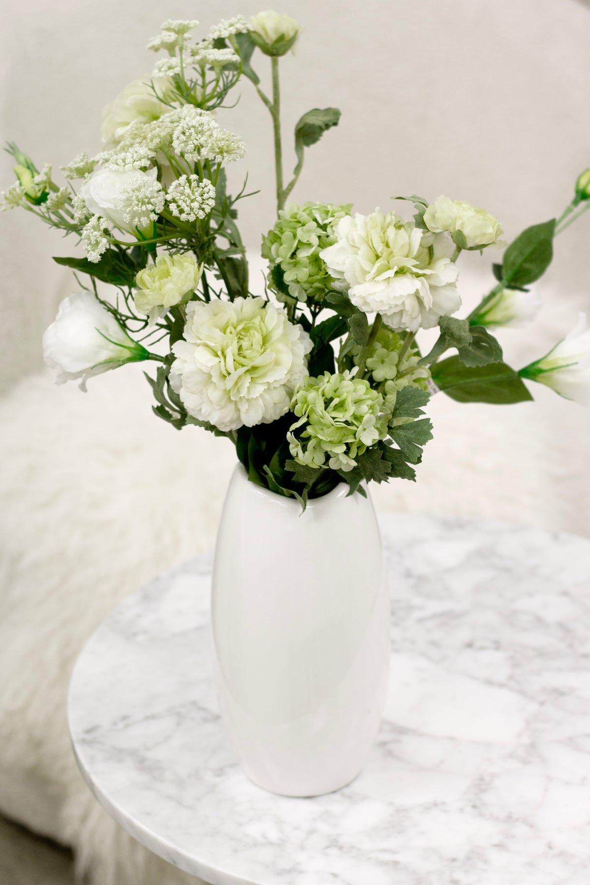 White Nordic vase of green carnations and gypsophila on a marble table with a soft sheepskin
