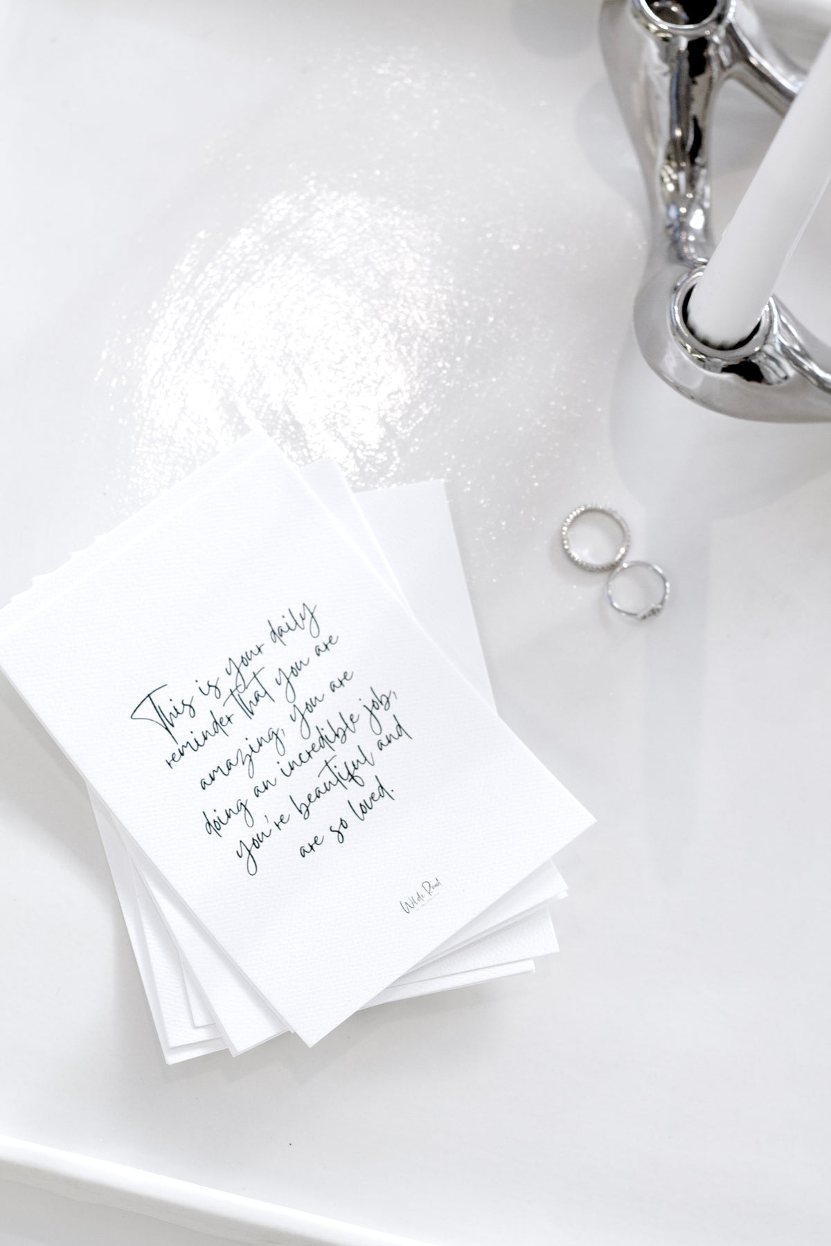 Stack of affirmation cards beside a white flower and rings