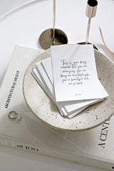 A textured stack of daily affirmation cards in a terrazzo-style bowl, with the top card reading: “This is your daily reminder that you are amazing, doing an incredible job, you’re beautiful and so loved.”