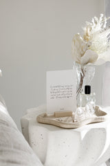 A set of affirmation cards displayed on a neutral bedside table with a wooden stand, dried floral arrangement, and perfume bottle styled in a soft, minimalist bedroom.