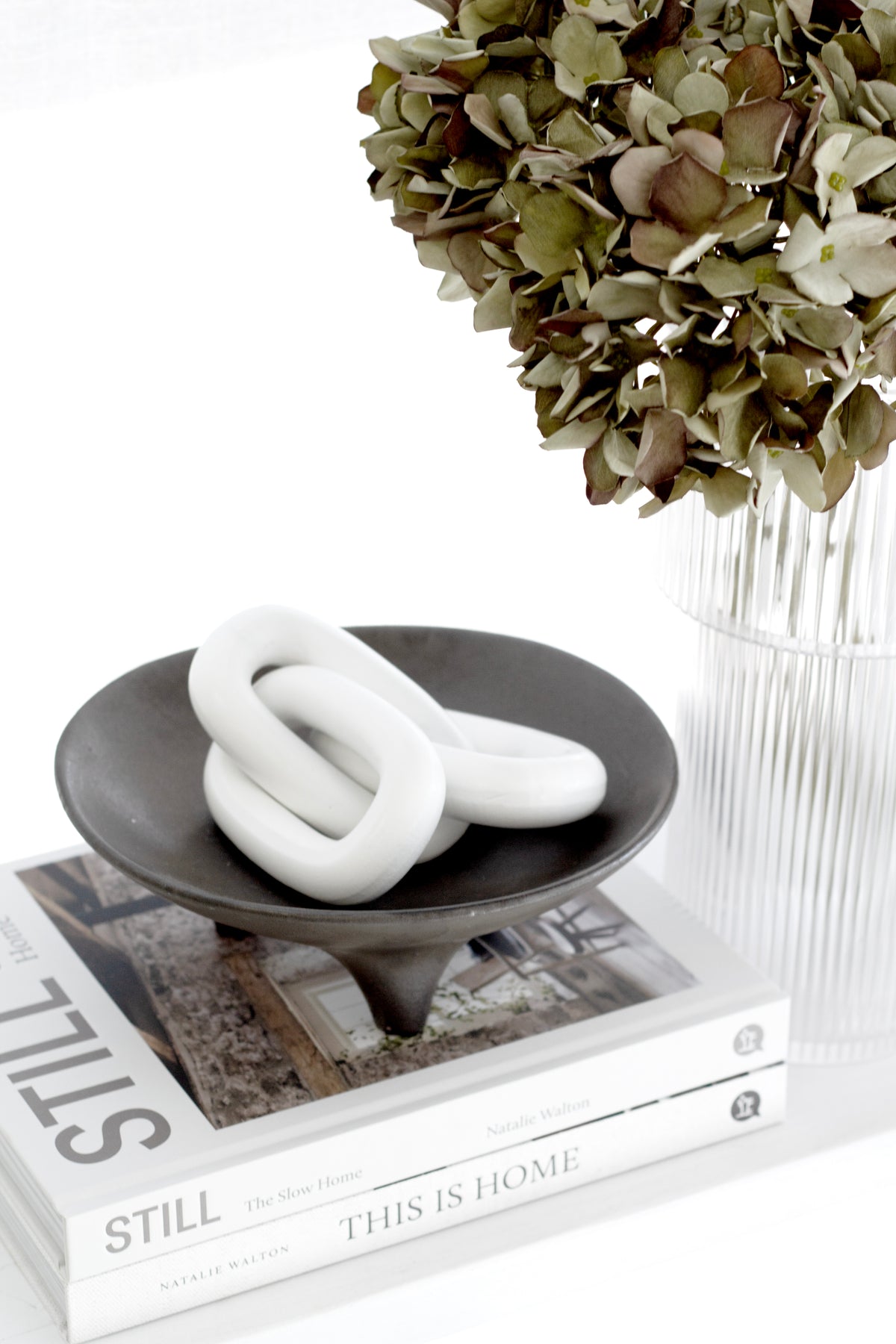 Onyx tripod plate holding a white knot ornament on books, beside dried hydrangea in a glass vase