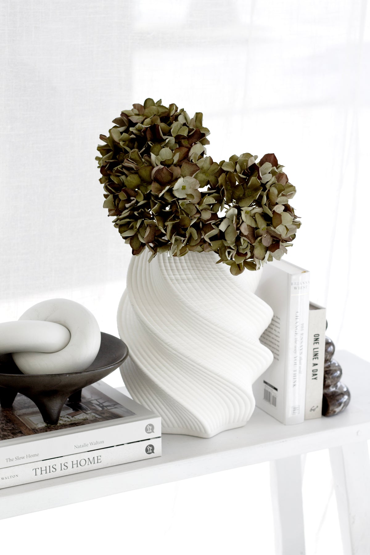 White 3D printed vase of dried hydrangea on a console with a knot sculpture and stacked books