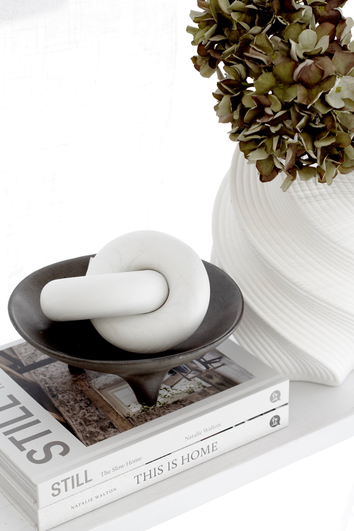 Close up of the white 3D printed vase with dried hydrangea beside a knot sculpture in a black dish