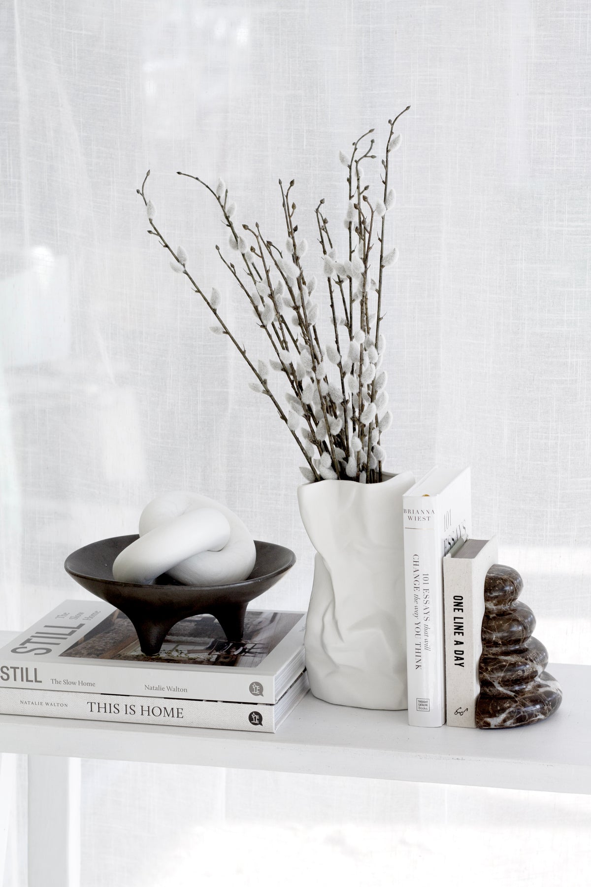 Onyx tripod plate of white stones on a shelf with a ribbed vase of pussy willow and books