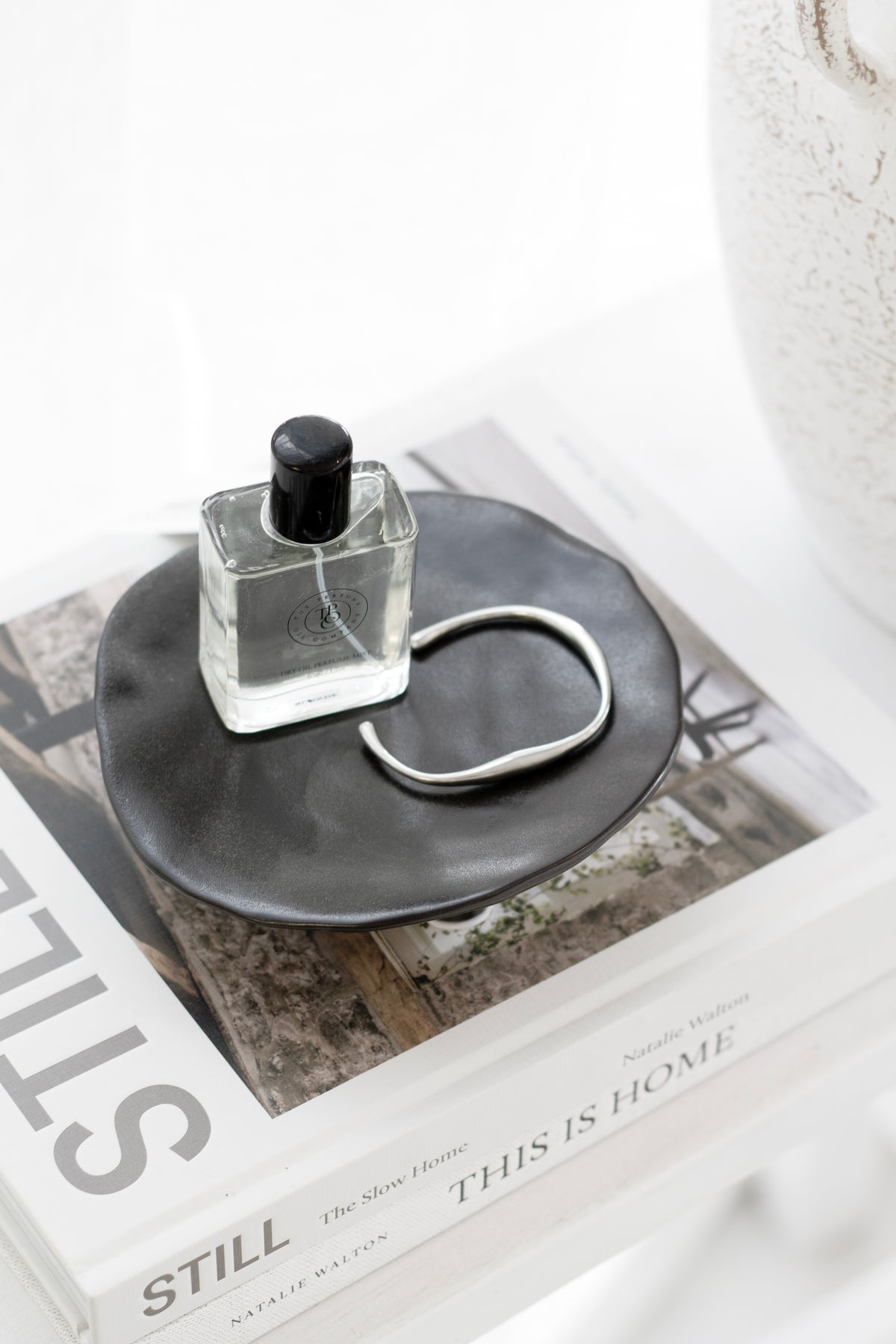 Black dish with a perfume bottle and a ring, set on a stack of interiors books