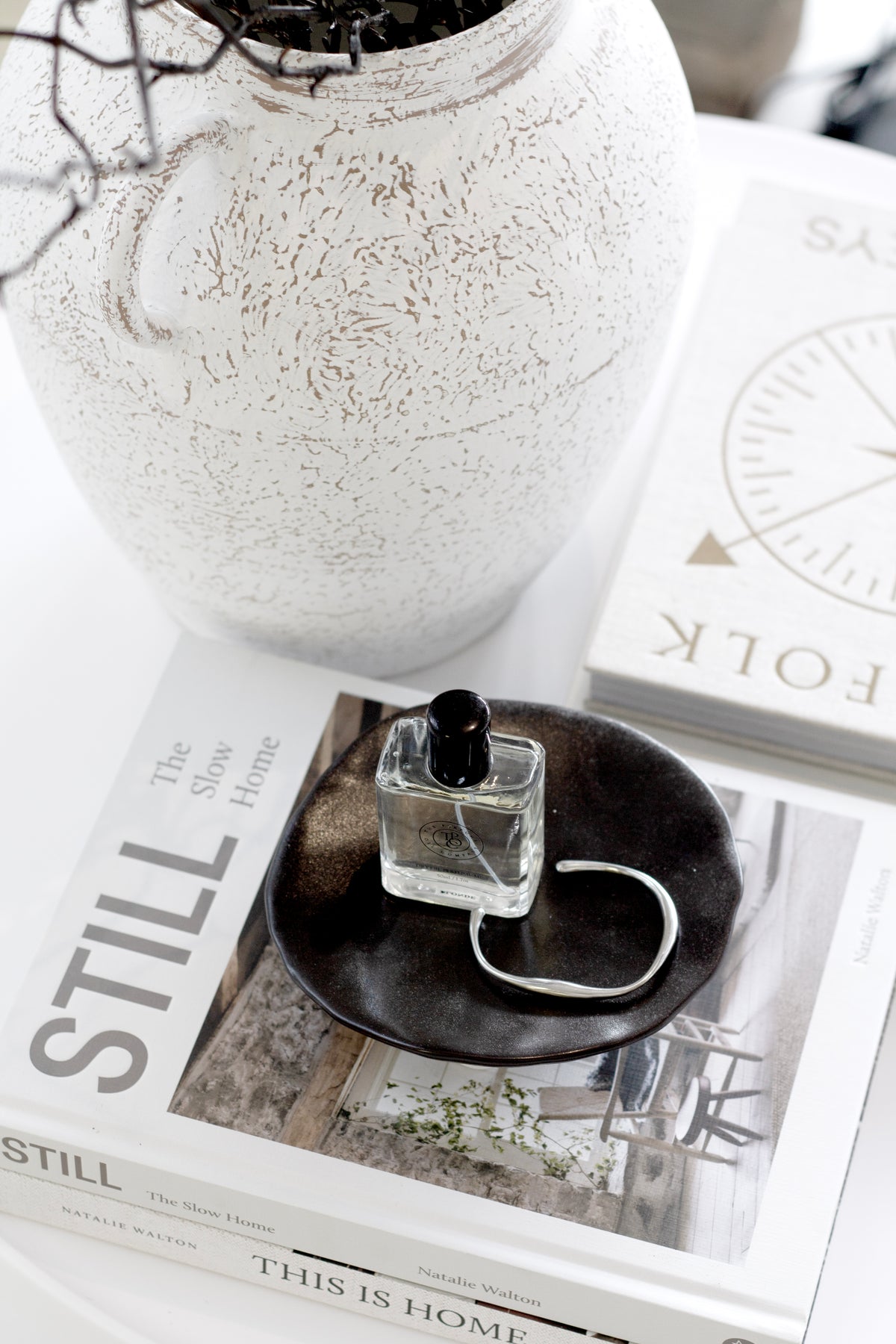 Looking down on the black dish of trinkets beside a speckled vase of dark stems