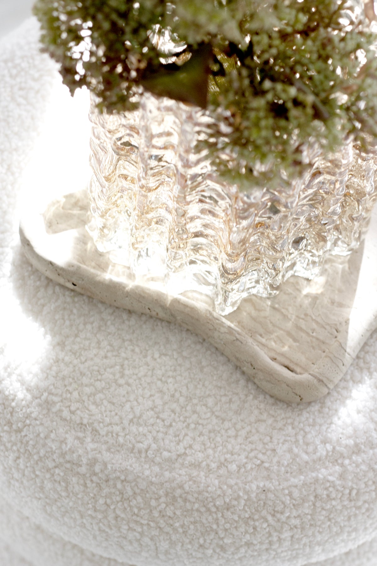 Textured white boucle beneath a cut glass vase of dried stems and driftwood