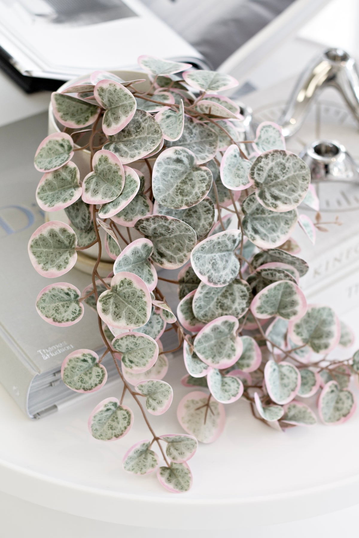 Faux variegated string of hearts spilling across a round white side table beside stacked books