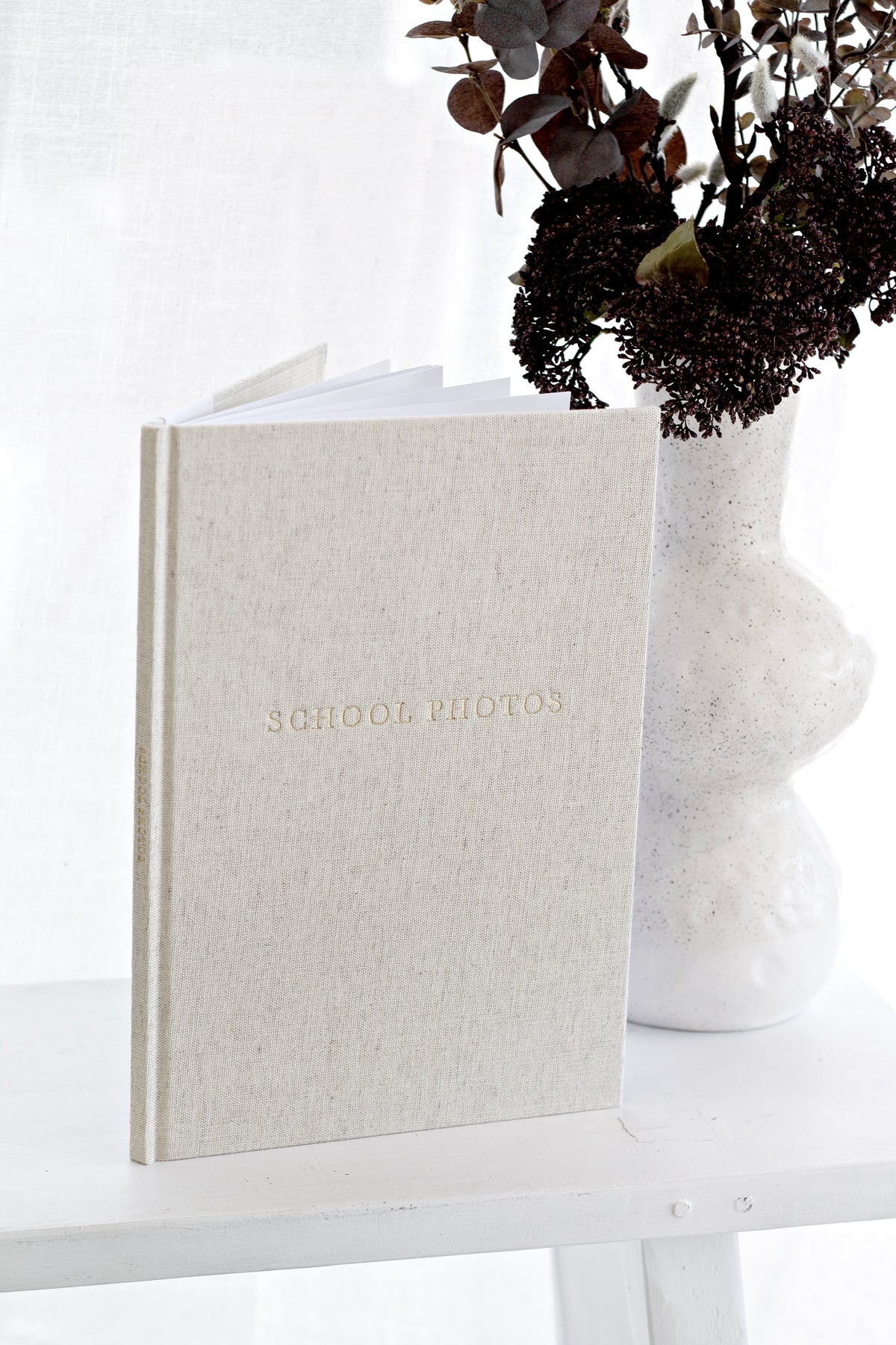 Oatmeal School Photos journal standing beside a white vase of dark foliage