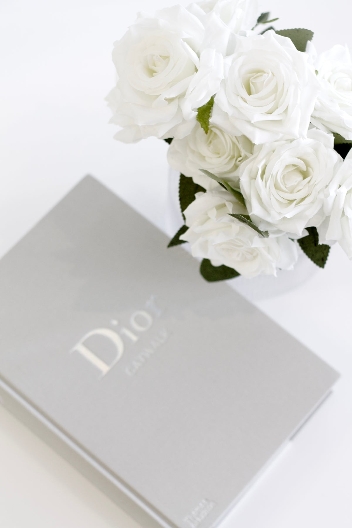 White roses in a glass vase above a grey coffee table book