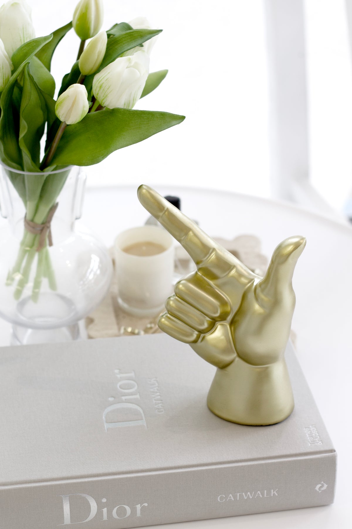Gold Lucky Hand on stacked books beside white tulips in a glass vase and a small candle