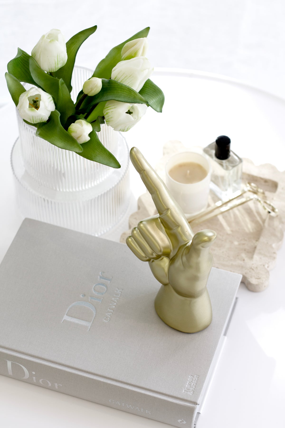 Gold Lucky Hand on books beside white tulips in a fluted vase and a fragrance bottle