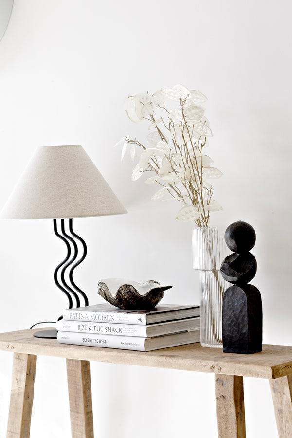 Natural Honesty Spray stem styled in a ribbed glass vase on a wooden console with black sculptural decor, design books, and a modern wavy lamp.