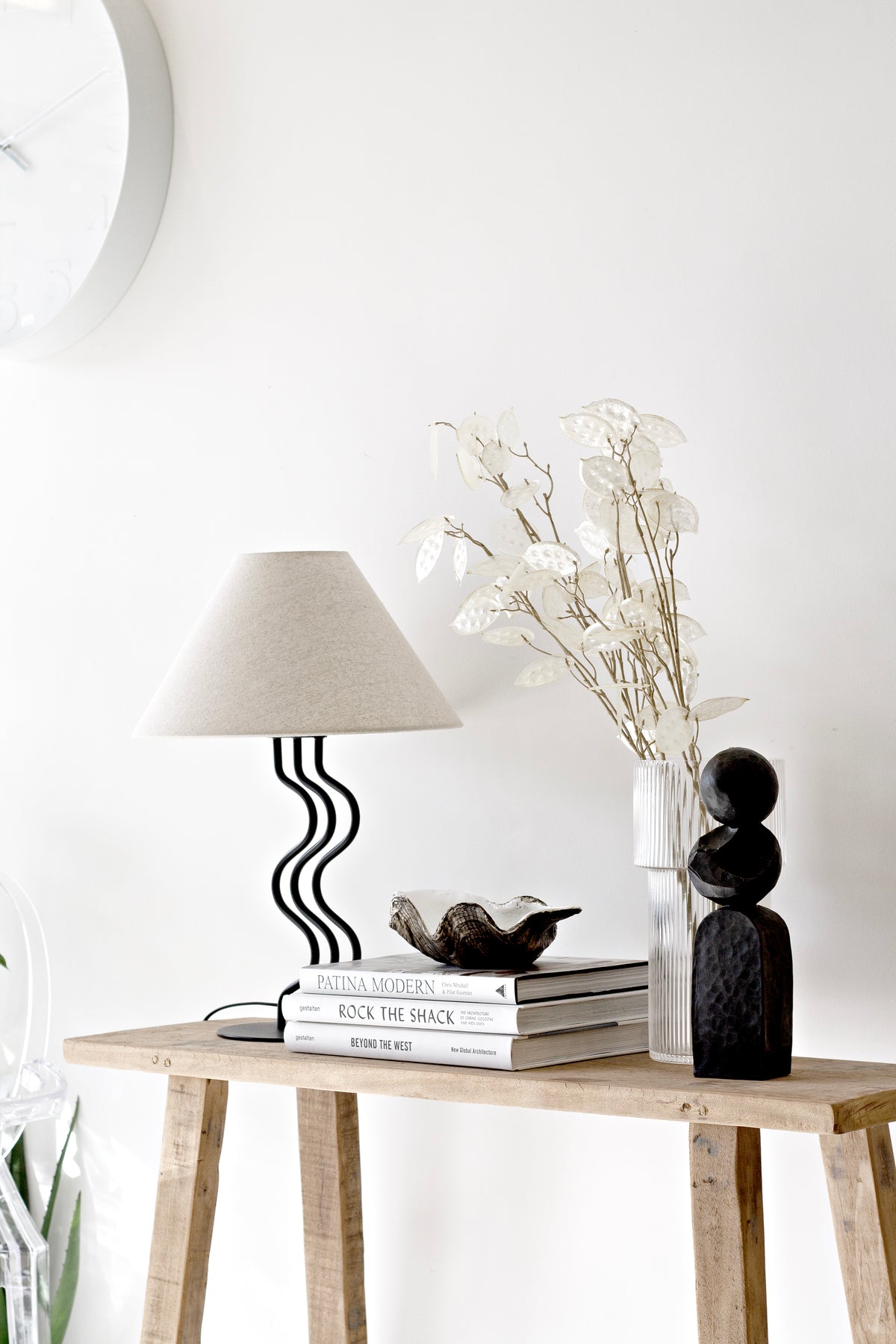 Black Pillar sculpture on a teak console with a wavy black lamp, dried stems and books