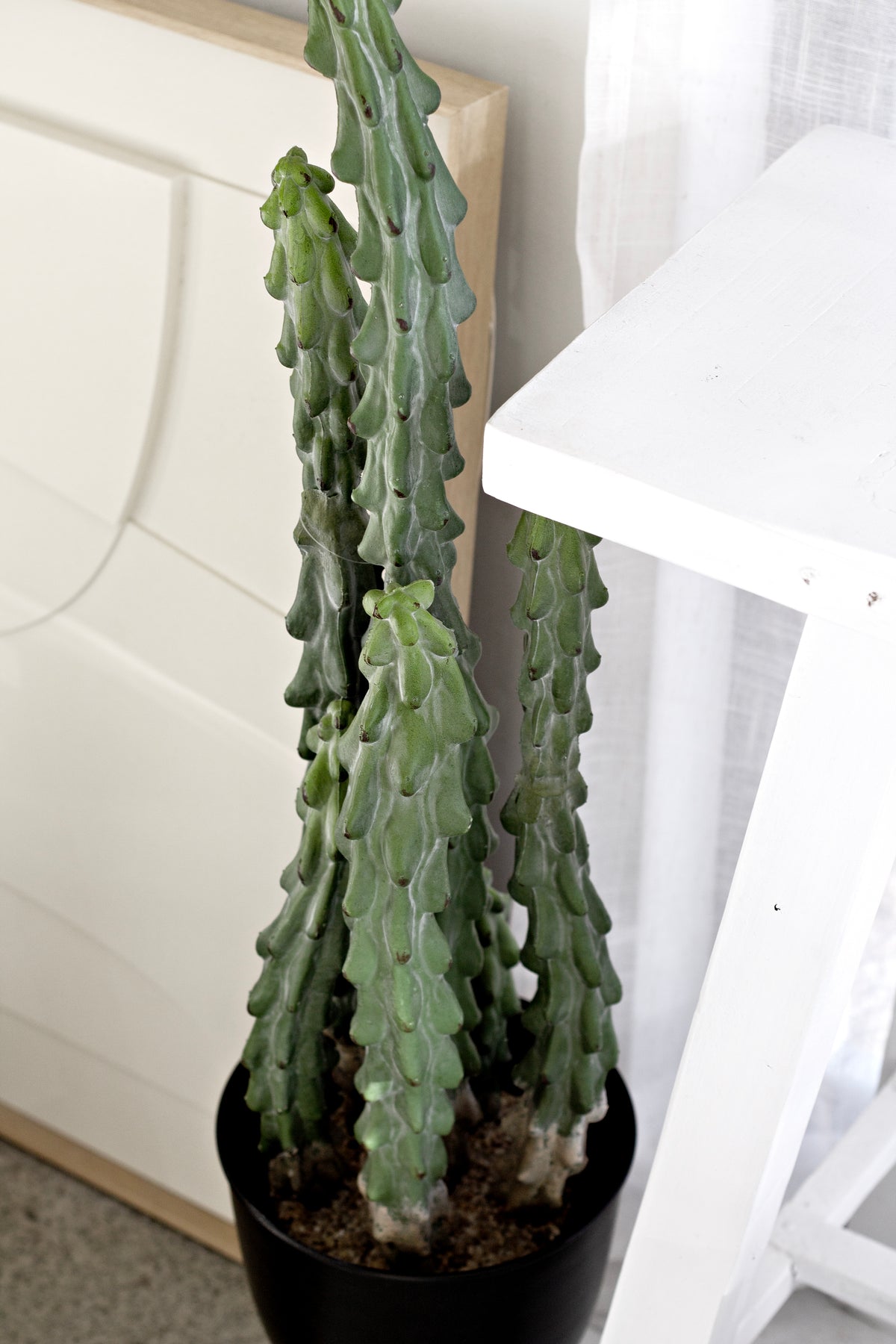 Tall faux cactus in a black pot beside a white table