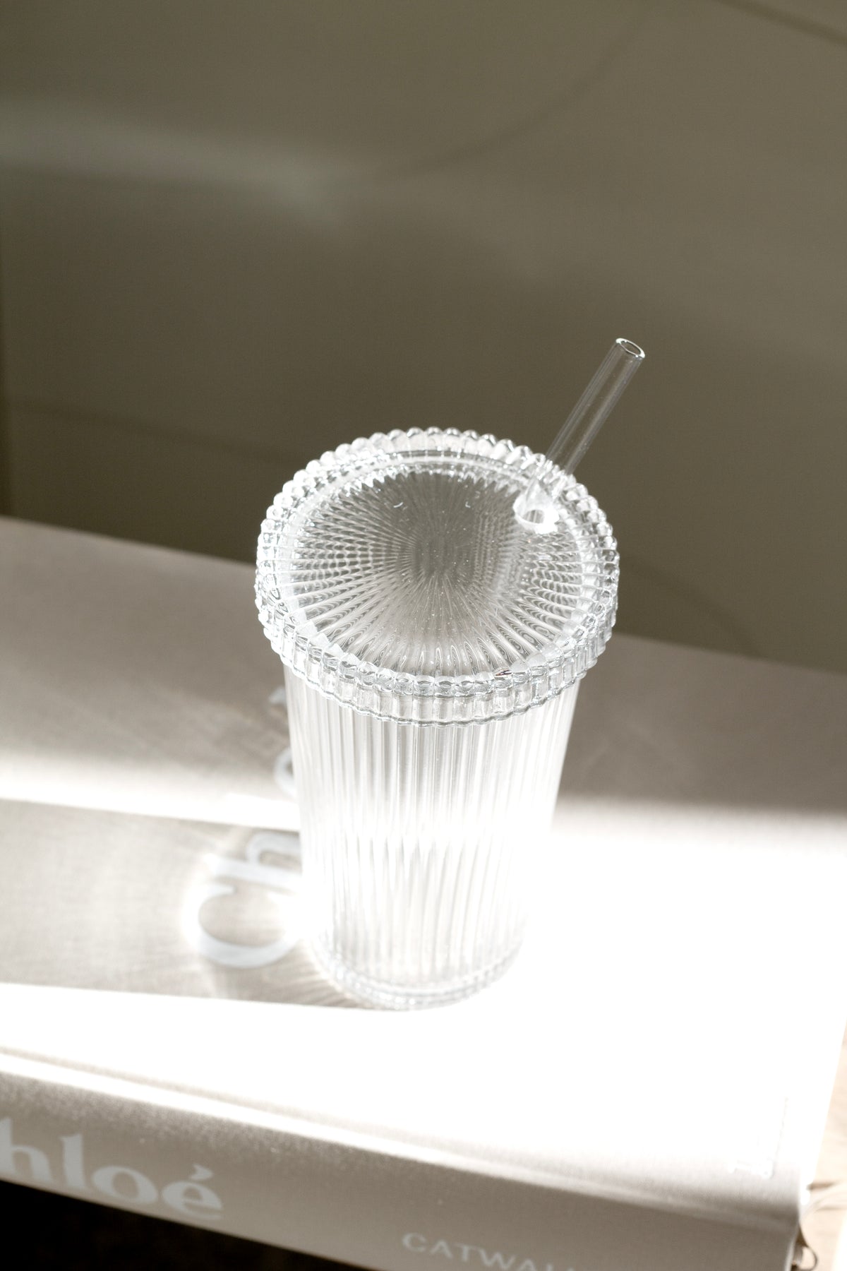 Ribbed glass tumbler with lid and glass straw styled on a shelf