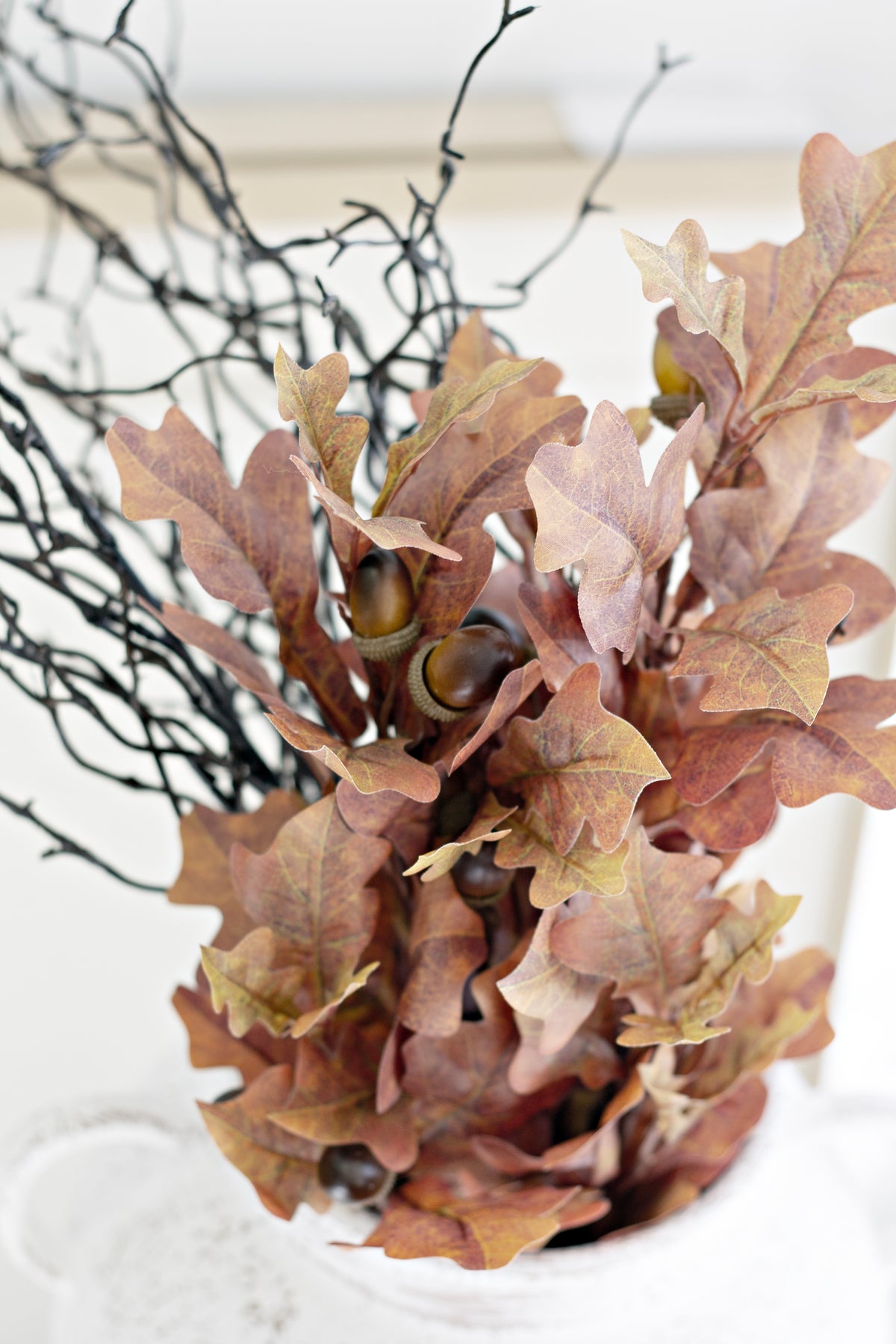 Faux oak leaf bush with dark curly branches in a white vase