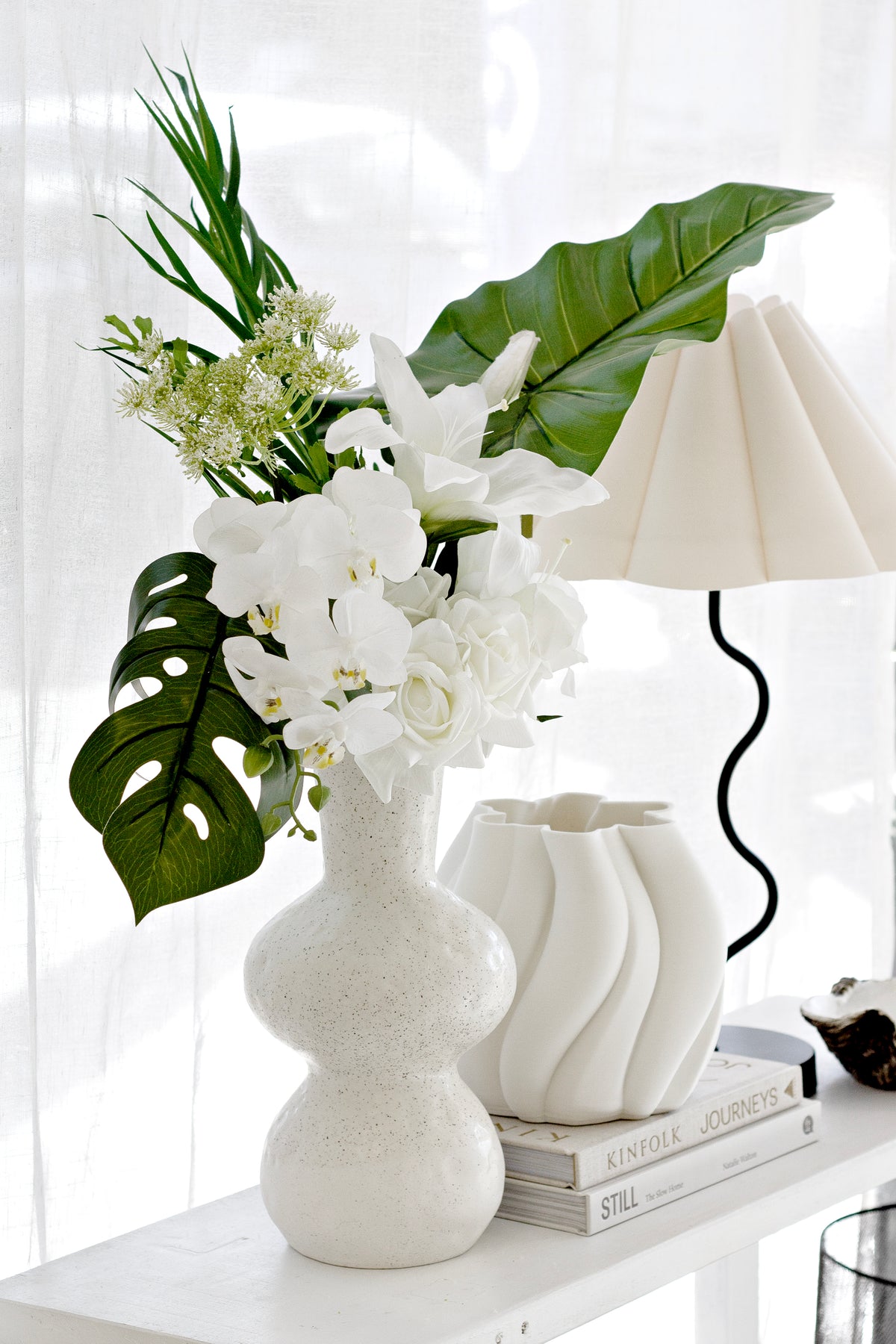 Dill ammi with white flowers and monstera leaves in a wavy vase beside a lamp