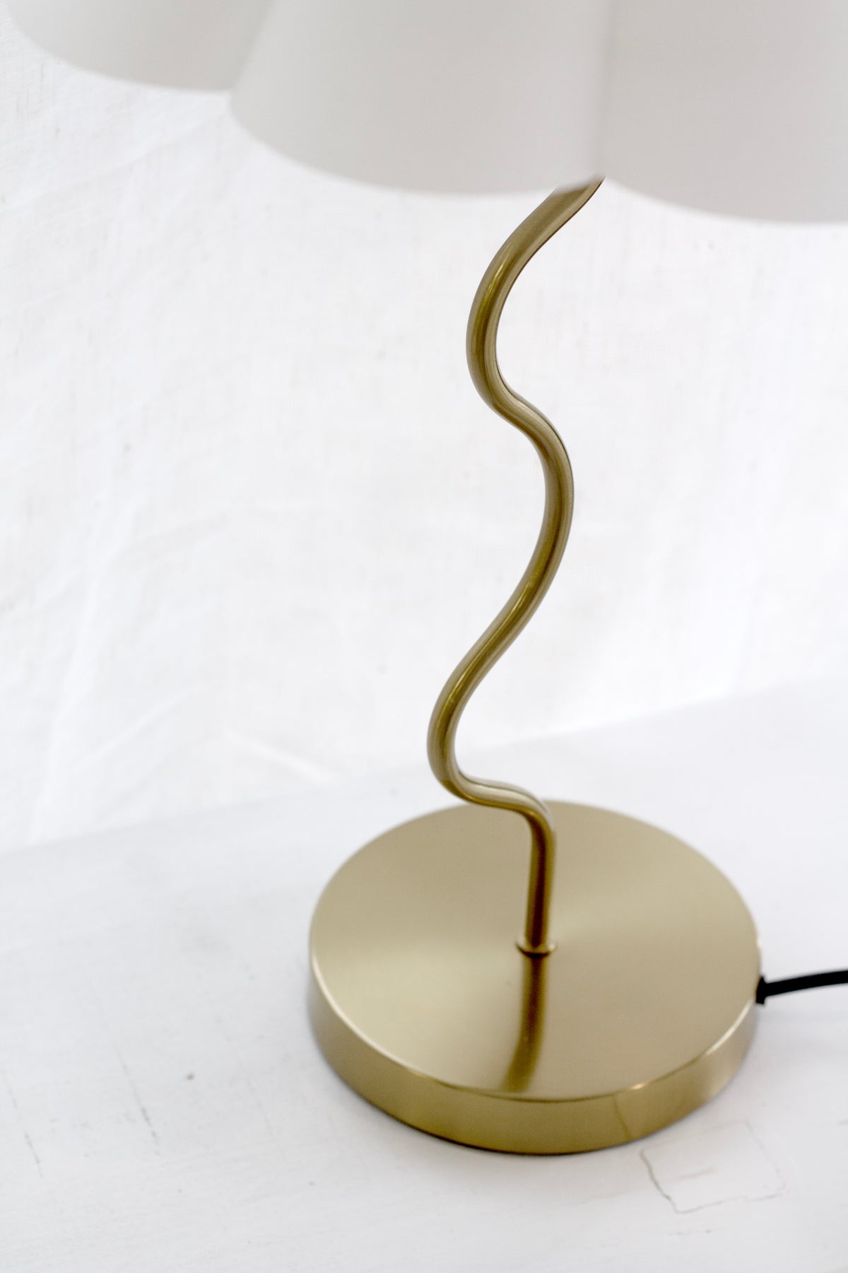 Close-up of the round brushed brass base and black cord on the Wavy table lamp