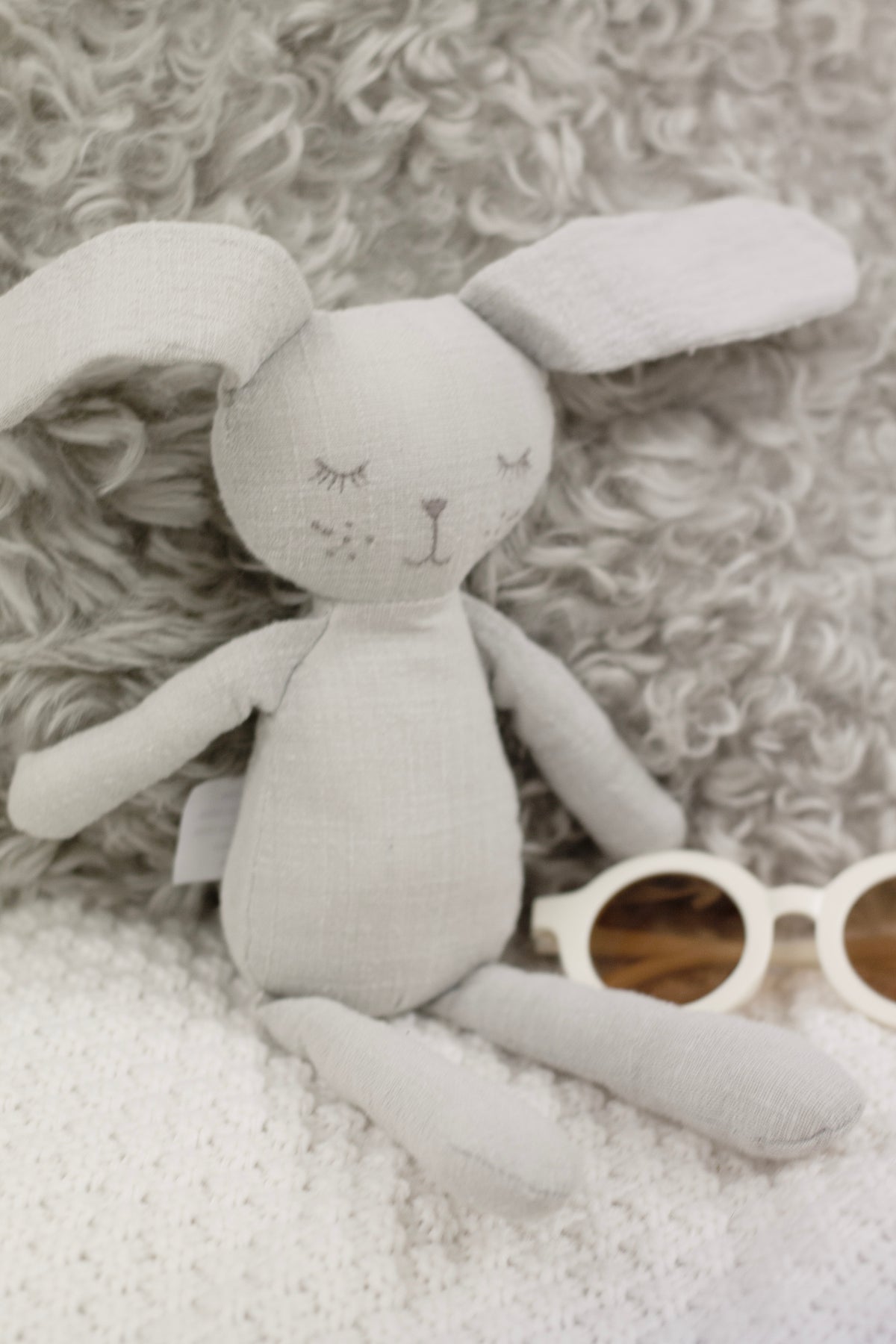 Close view of Grey the Bunny in soft grey linen with stitched closed eyes, on a sheepskin