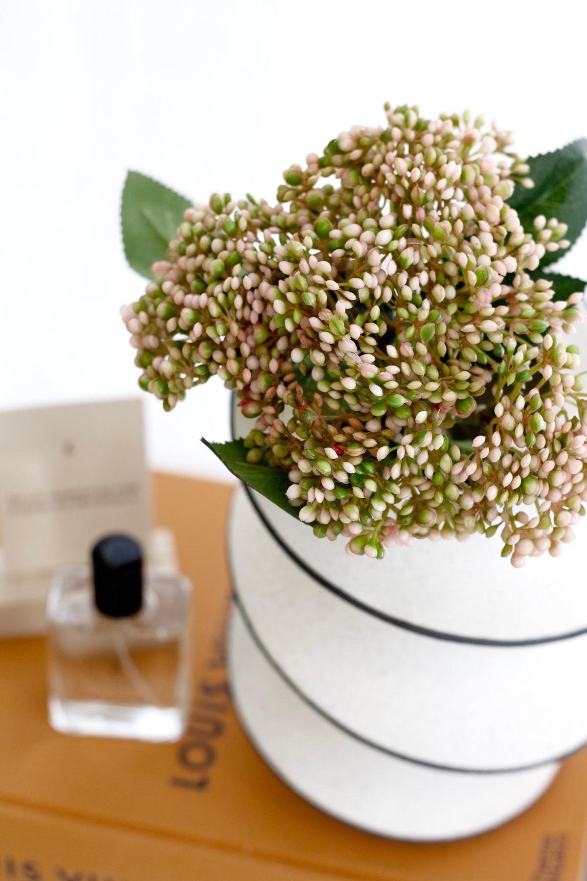 Close view of green hydrangea in the spiral ceramic vase beside a perfume bottle