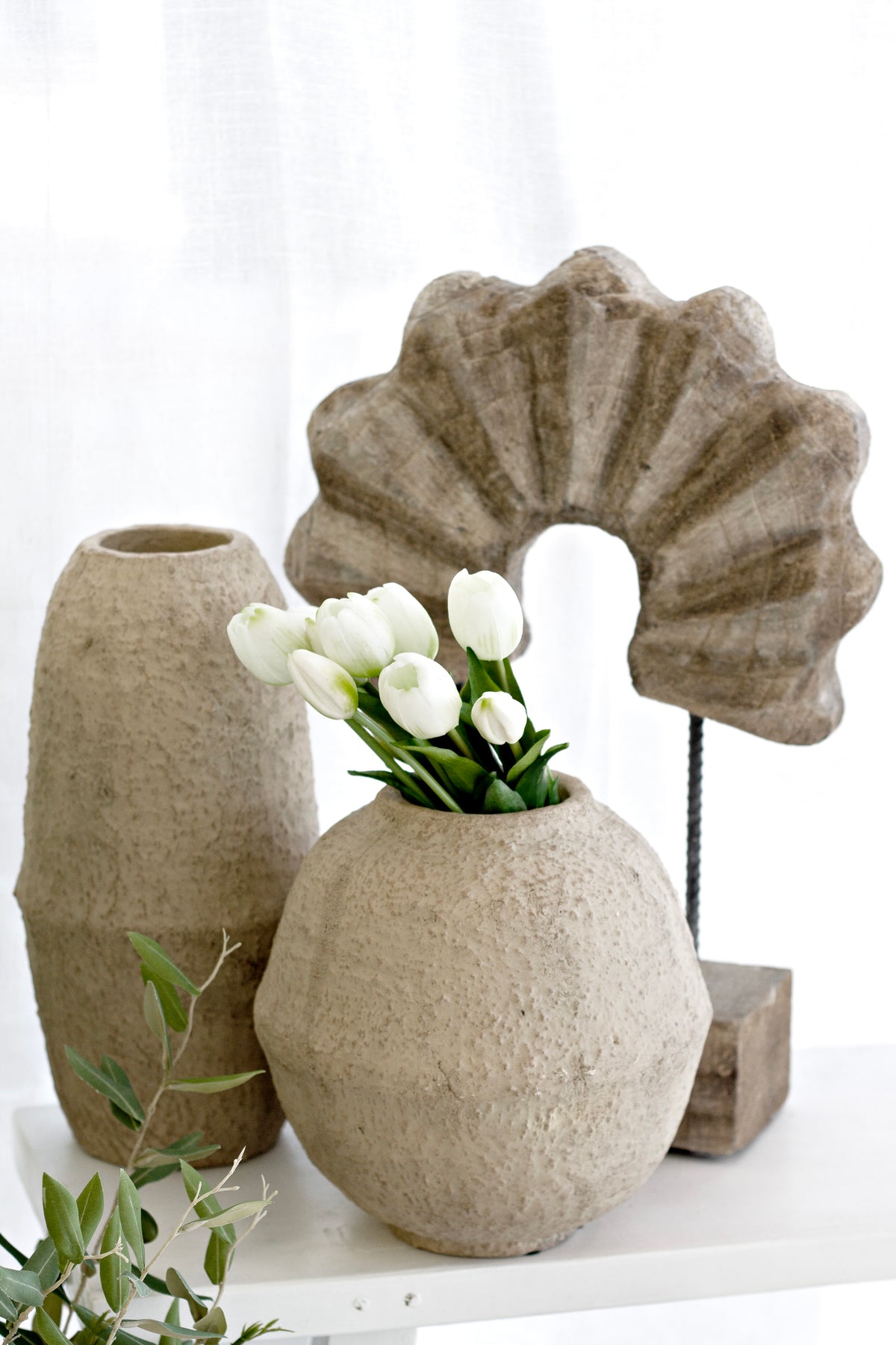 Timber arch sculpture beside a tall textured vase and a round vase of white tulips