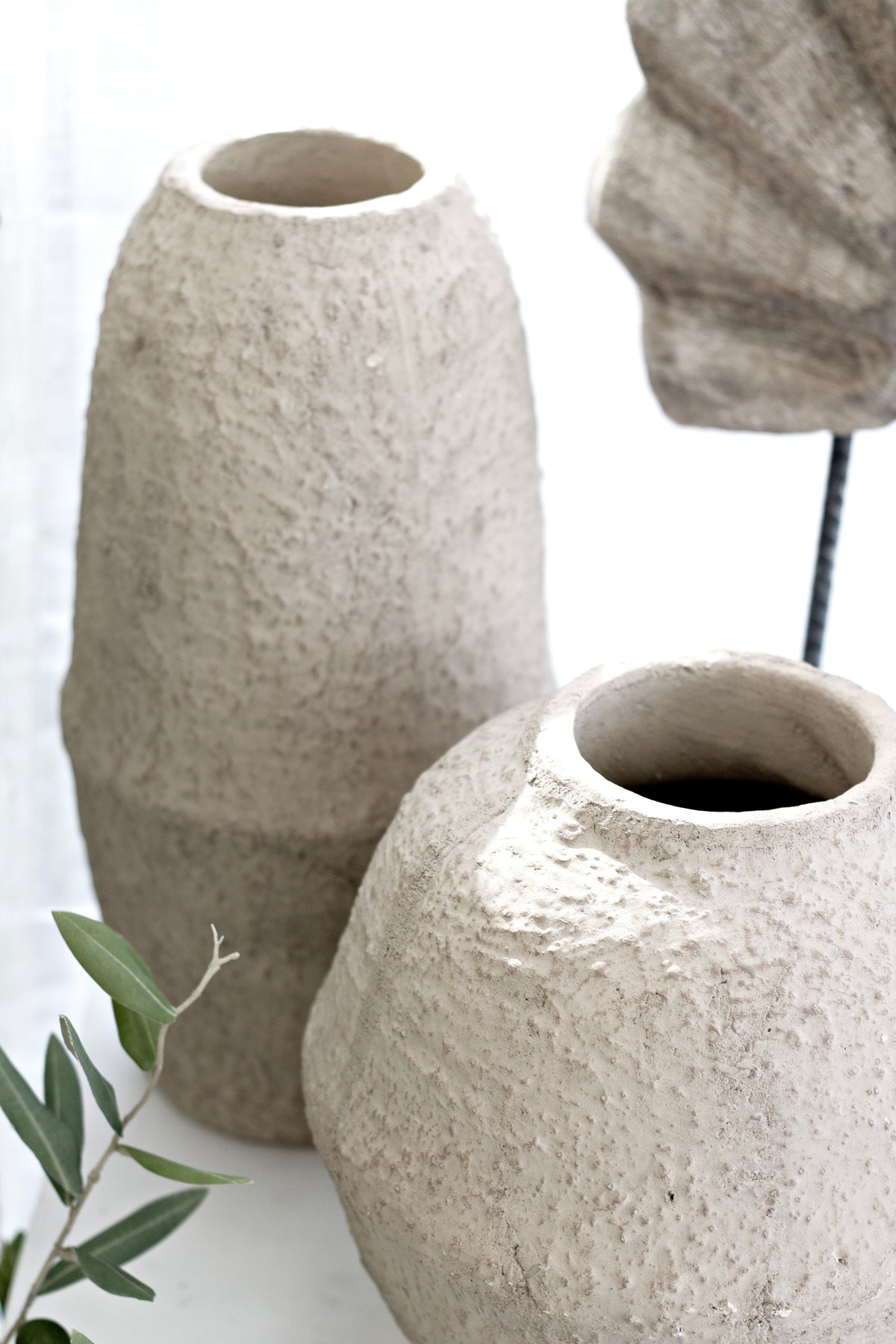 Joni vase paired with a taller sand vase, with a timber arch sculpture and olive stems behind