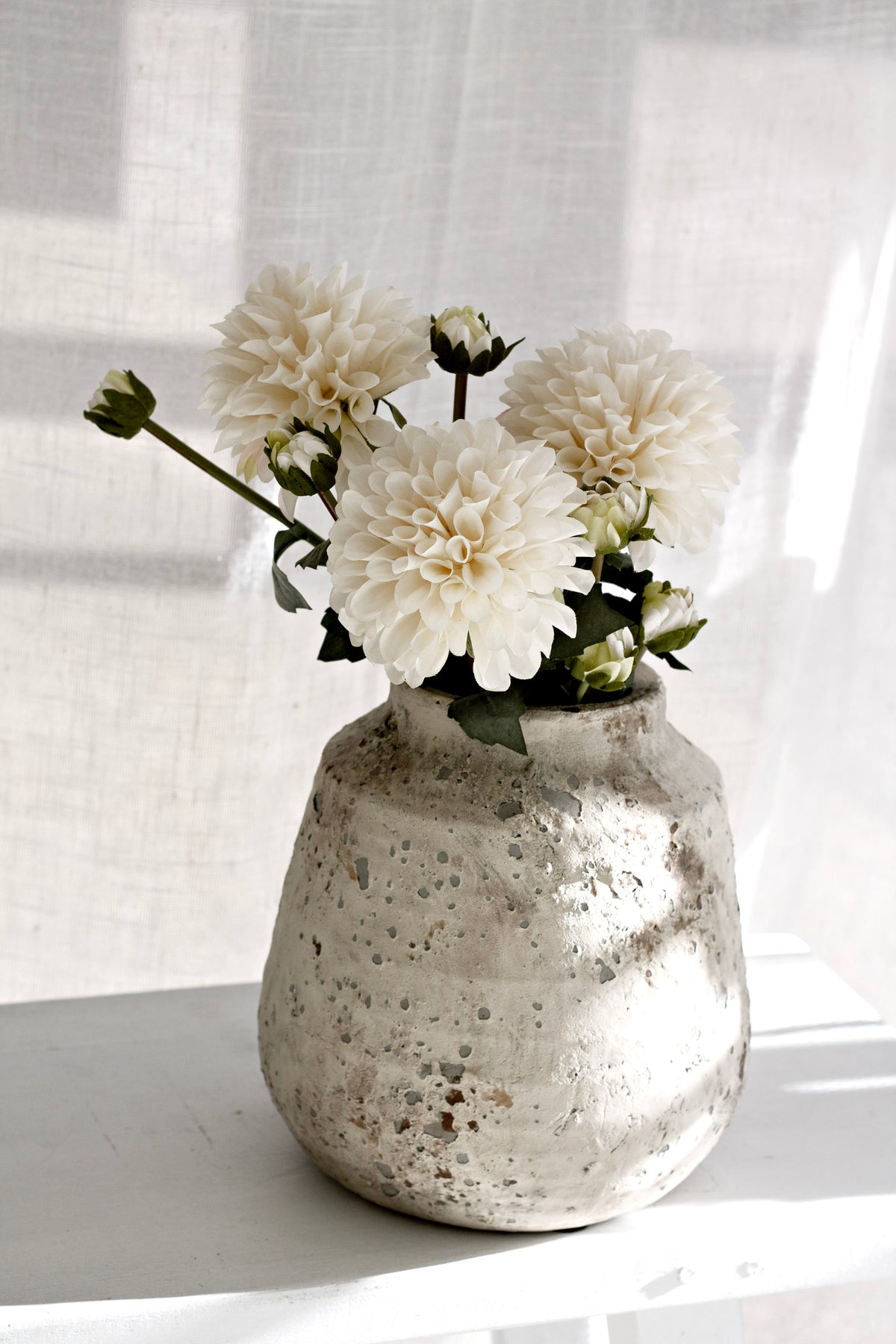 Dahlias with buds in a speckled vase on a white table in strong afternoon sun