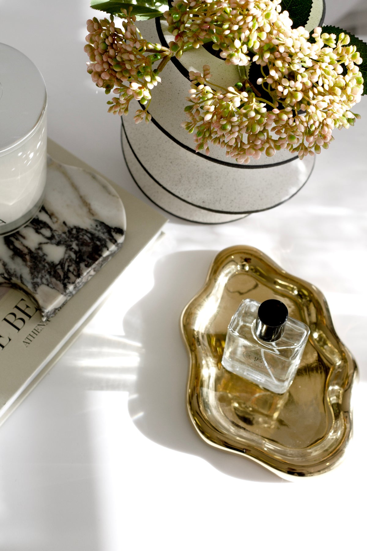 Spiral ceramic vase of dried blossom beside a gold shell dish holding a perfume bottle